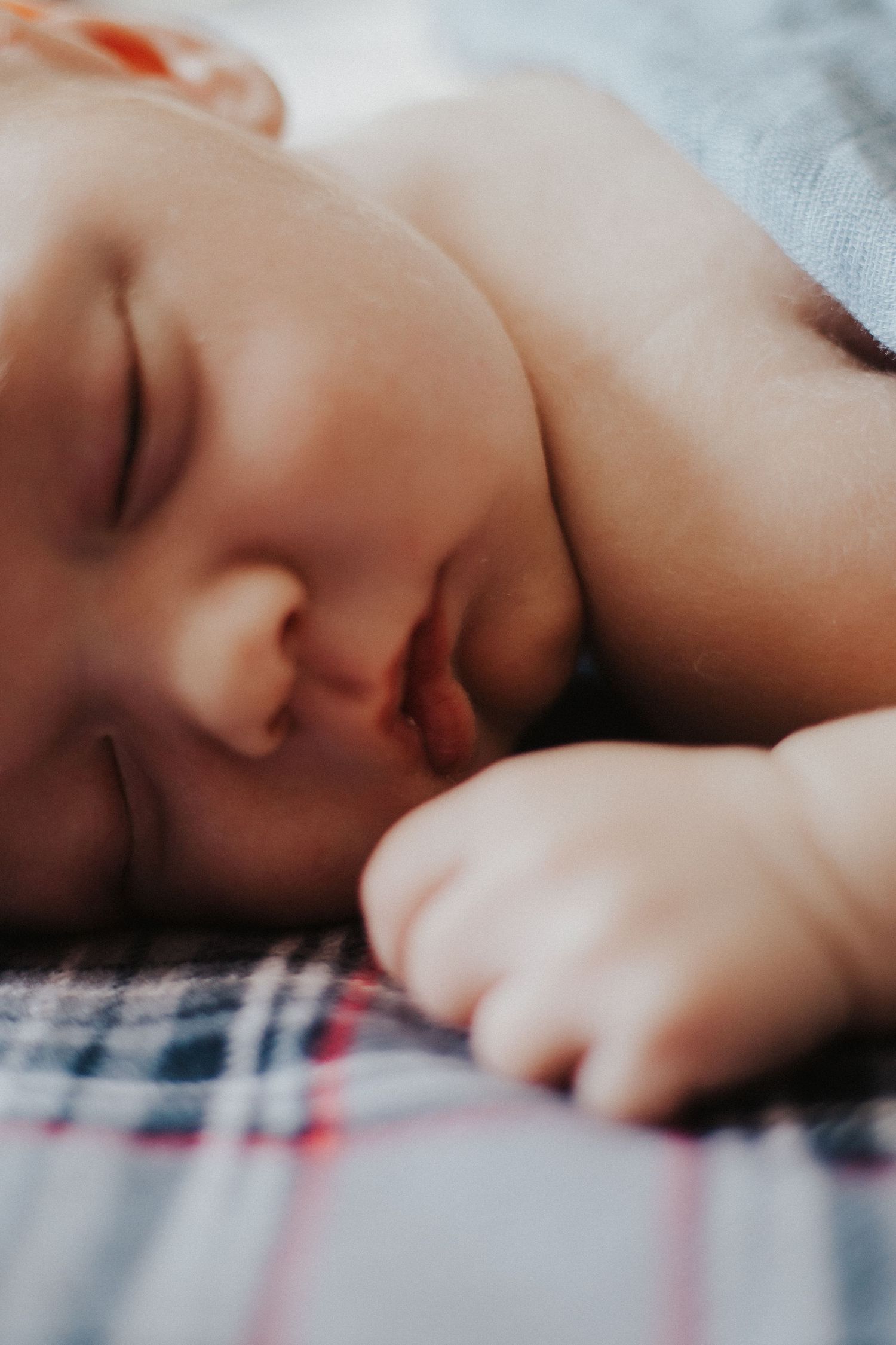 baby boy sleeps on his stomach on a plaid blanket