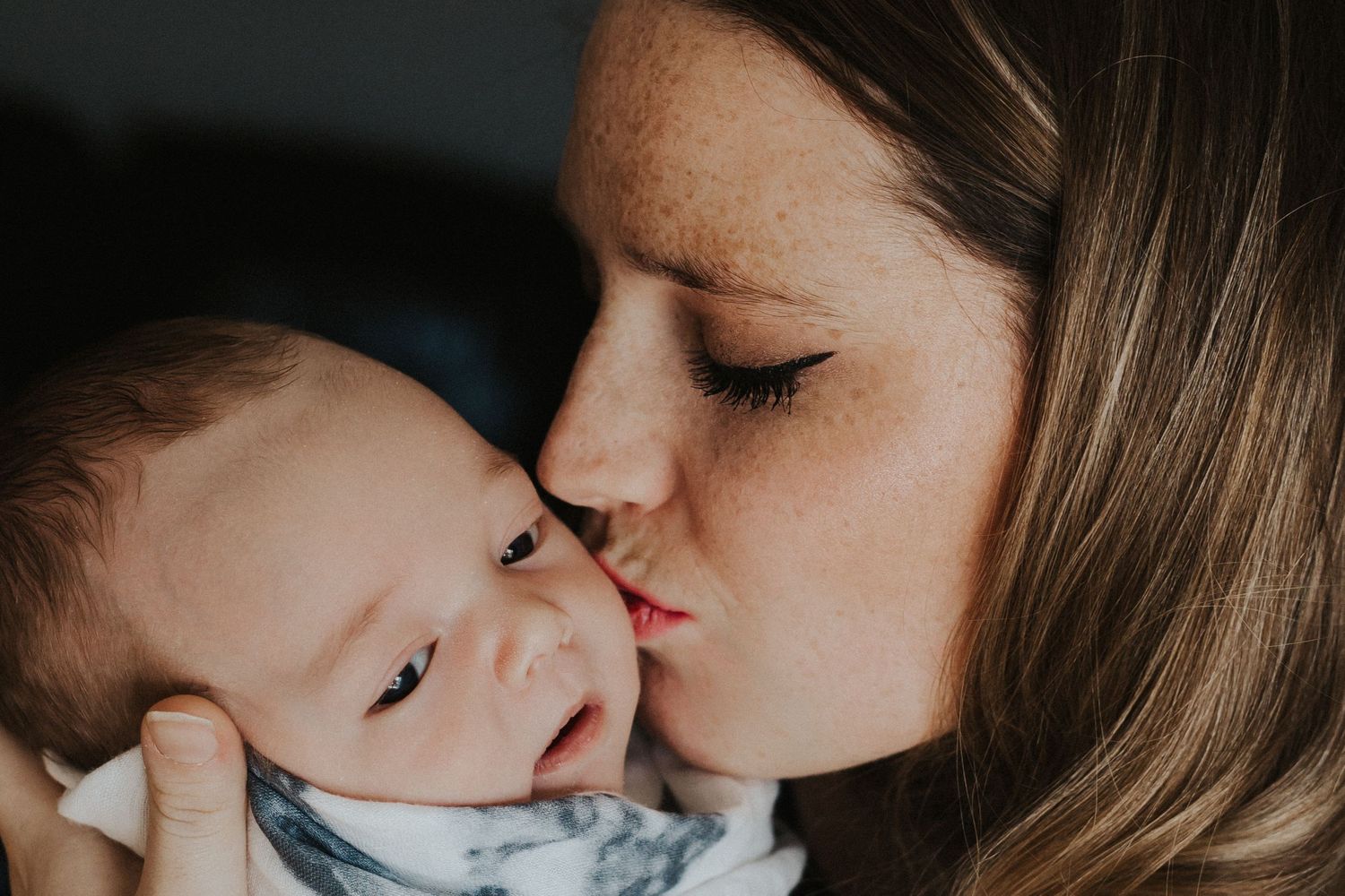 mother kisses baby boy on the cheek while holding him in her arms