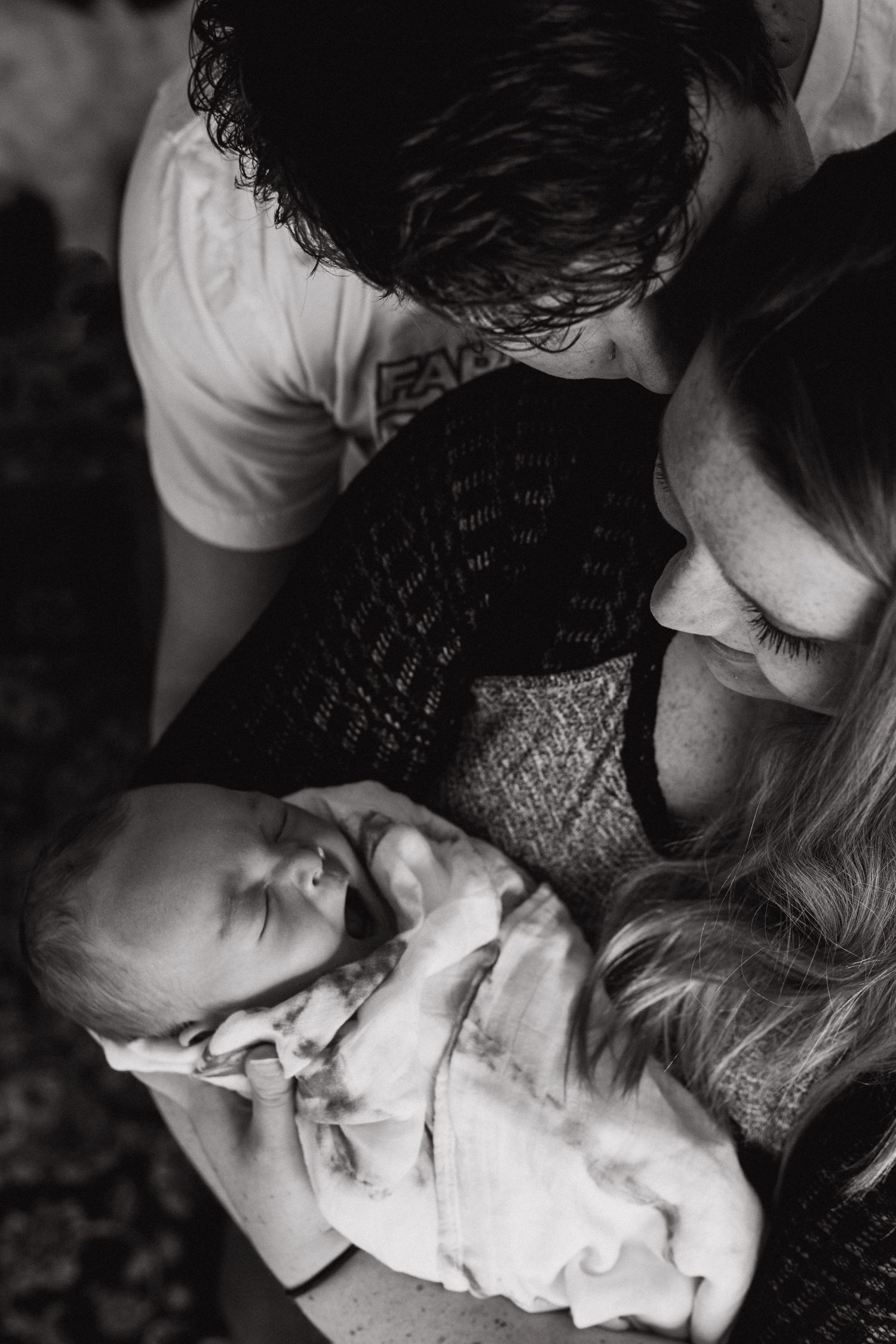 Husband kisses his wife on the cheek while they both look down at their baby boy