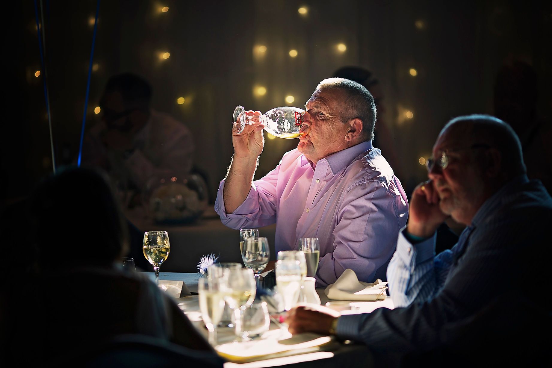 Male guest drinks a pint of lager under a spotlight inside Bolton School wedding venue