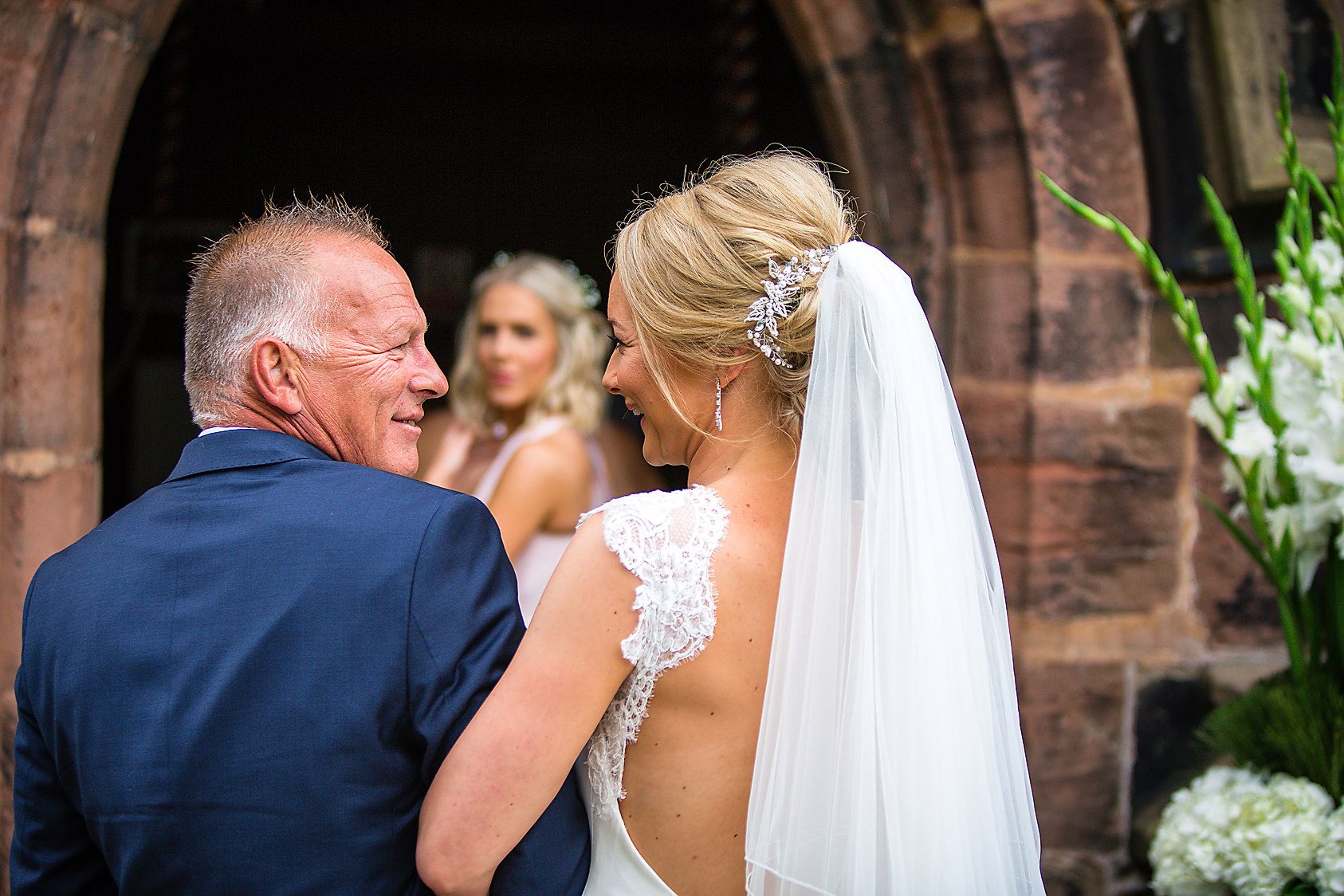 Father of brides looks proudly at his daughter, watched by bridesmaids at the church entrance