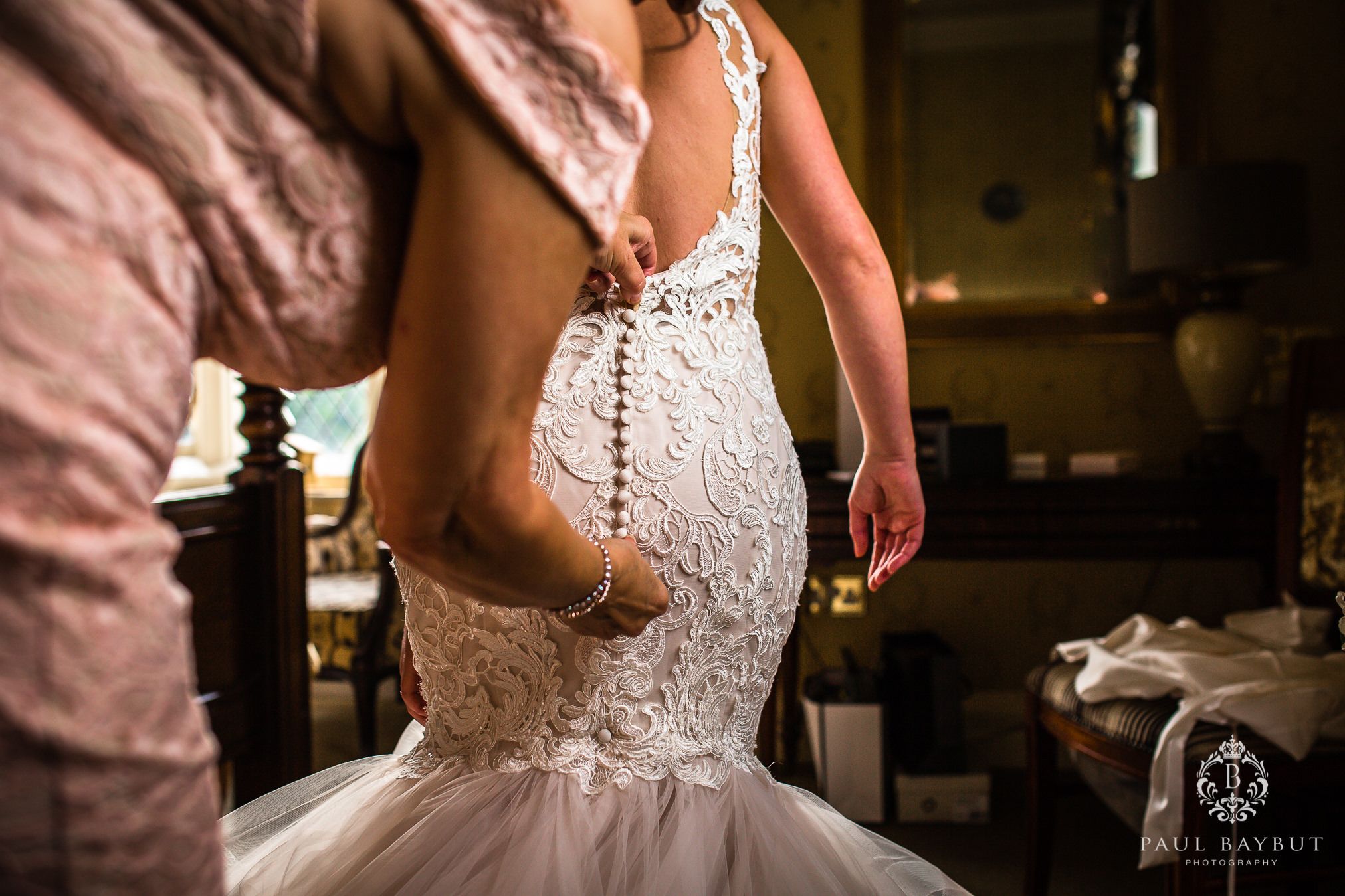 Mother button up the back of a brides wedding dress in a bedroom at Crewe Hall wedding venue