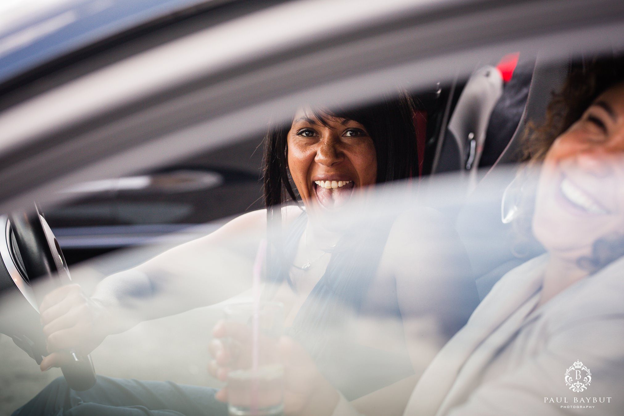 Two female wedding guests laugh from inside a car at Gorton Monastery wedding venue