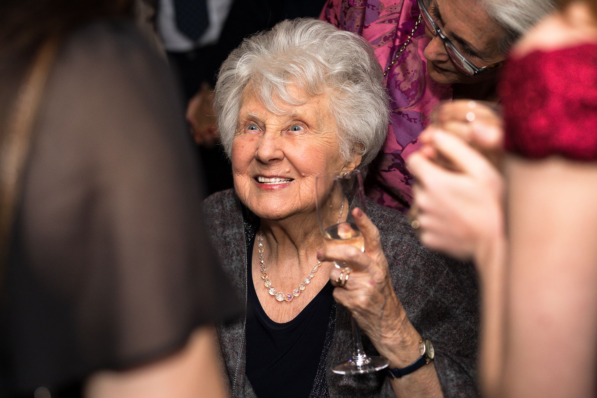 Grandmother of the bride smiles during indoor wedding celebrations amongst female guests