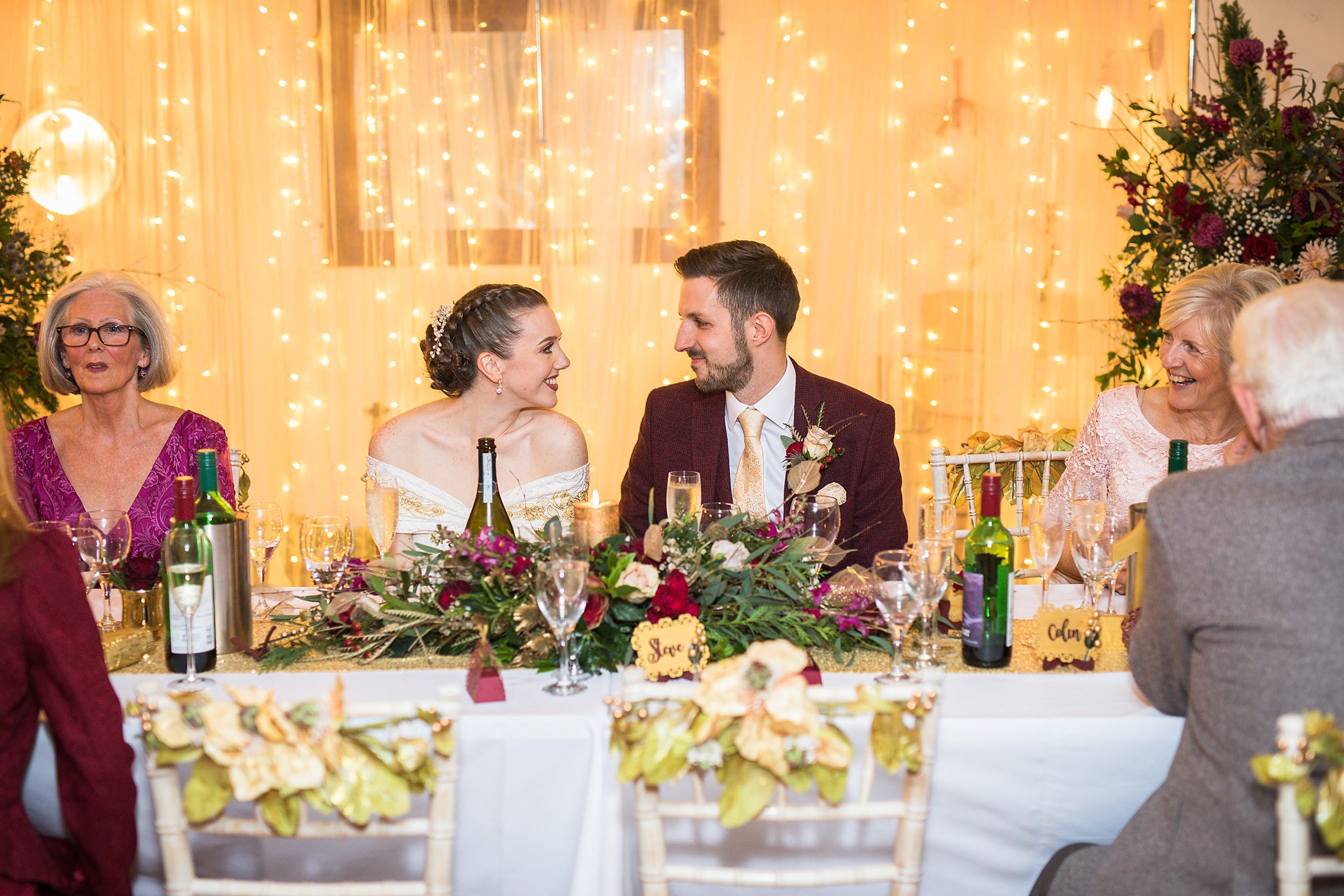 Bride and groom sat at their wedding table look adoringly into each others eyes surrounded by seated guests