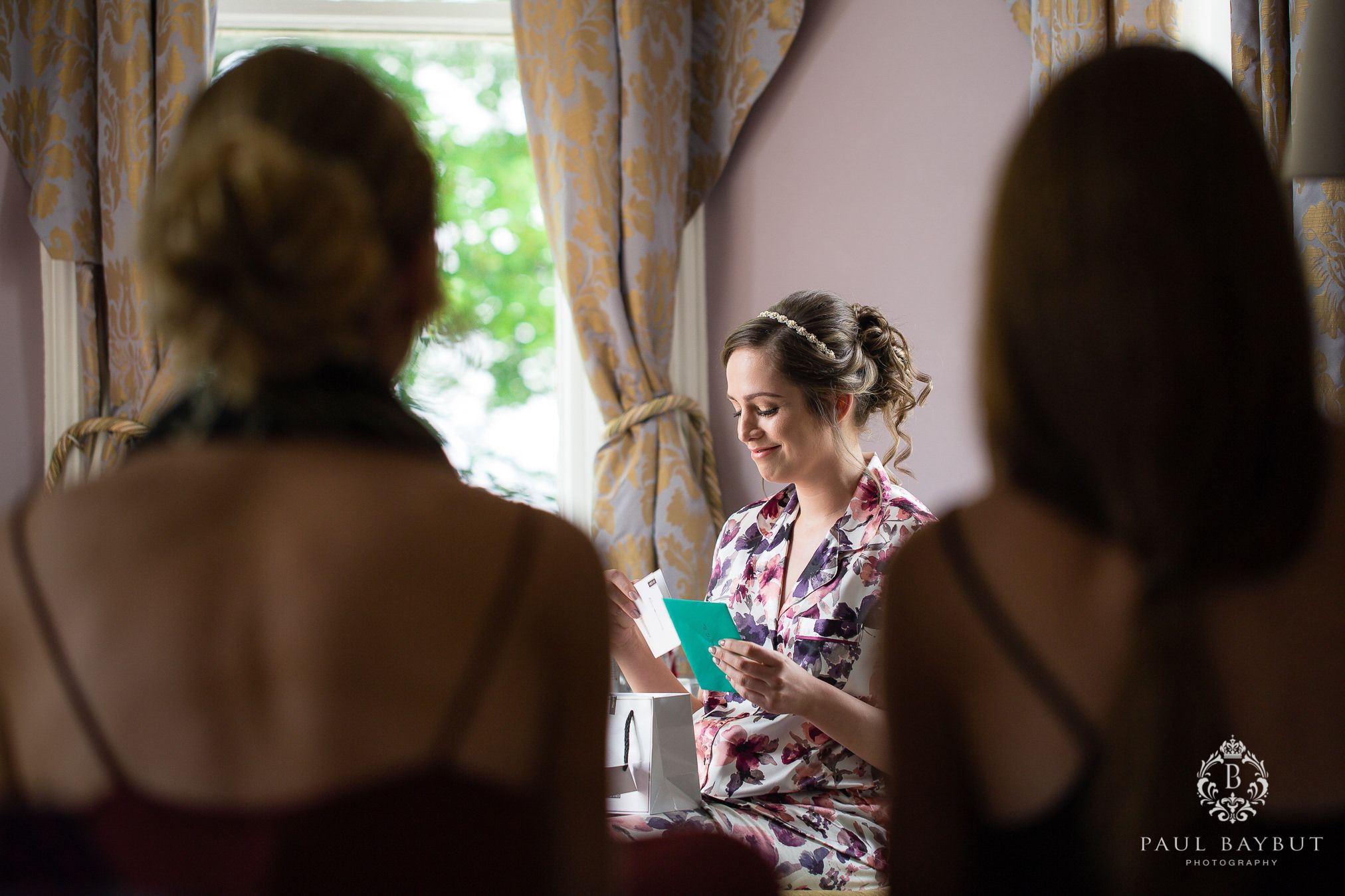Bridesmaids watch a delighted bride as she reads a message in a card during bridal prep at Hollin House Hotel