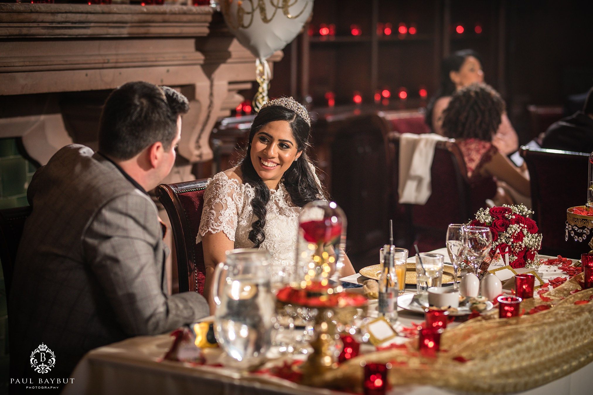 Smiling bride looks at her groom whilst seated at their wedding breakfast table in the great hall of Peckforton Castle