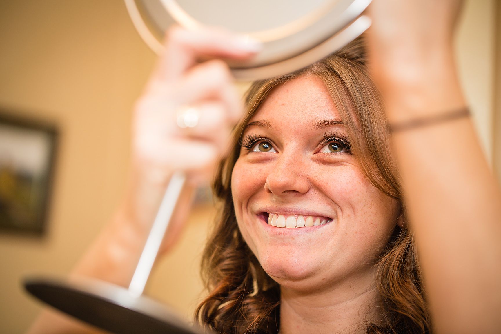 Bridesmaid looks at her face in a hand mirror during bridal preparations in the brides house