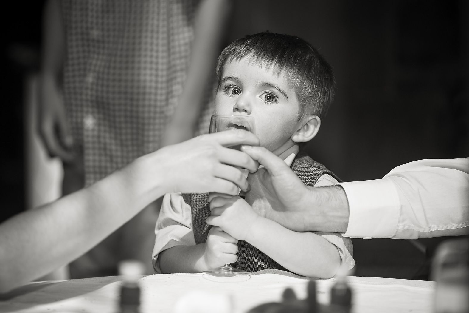Parents try and take a glass of wine away from their small boy at the wedding table