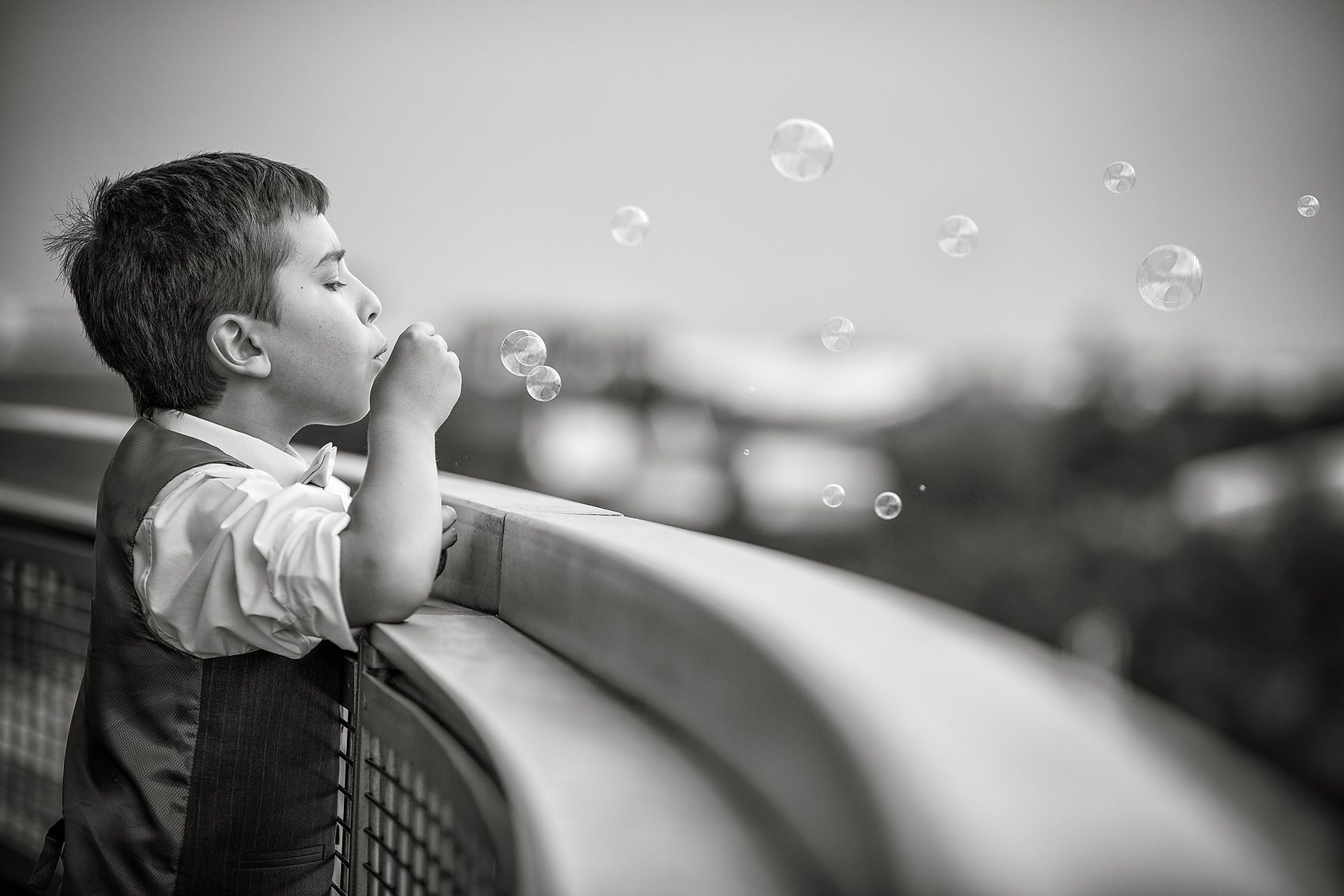 Young boy wearing a waistcoat blows bubbles over the balcony of The Lowry in Manchester