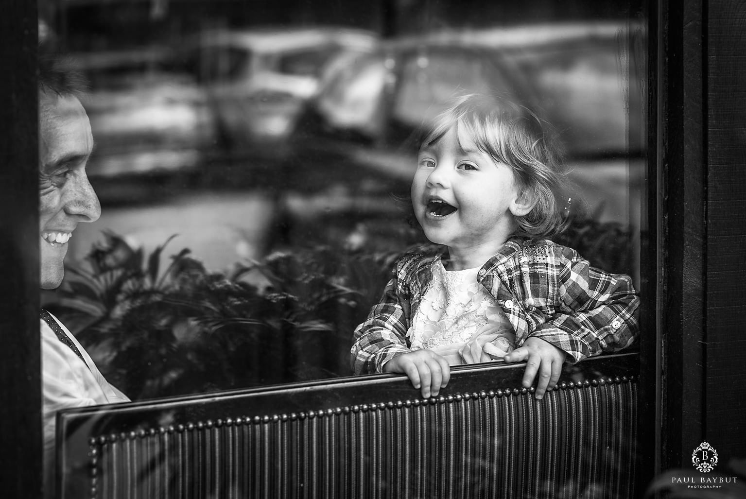 Little girl laughs heartily with her father behind a glass window