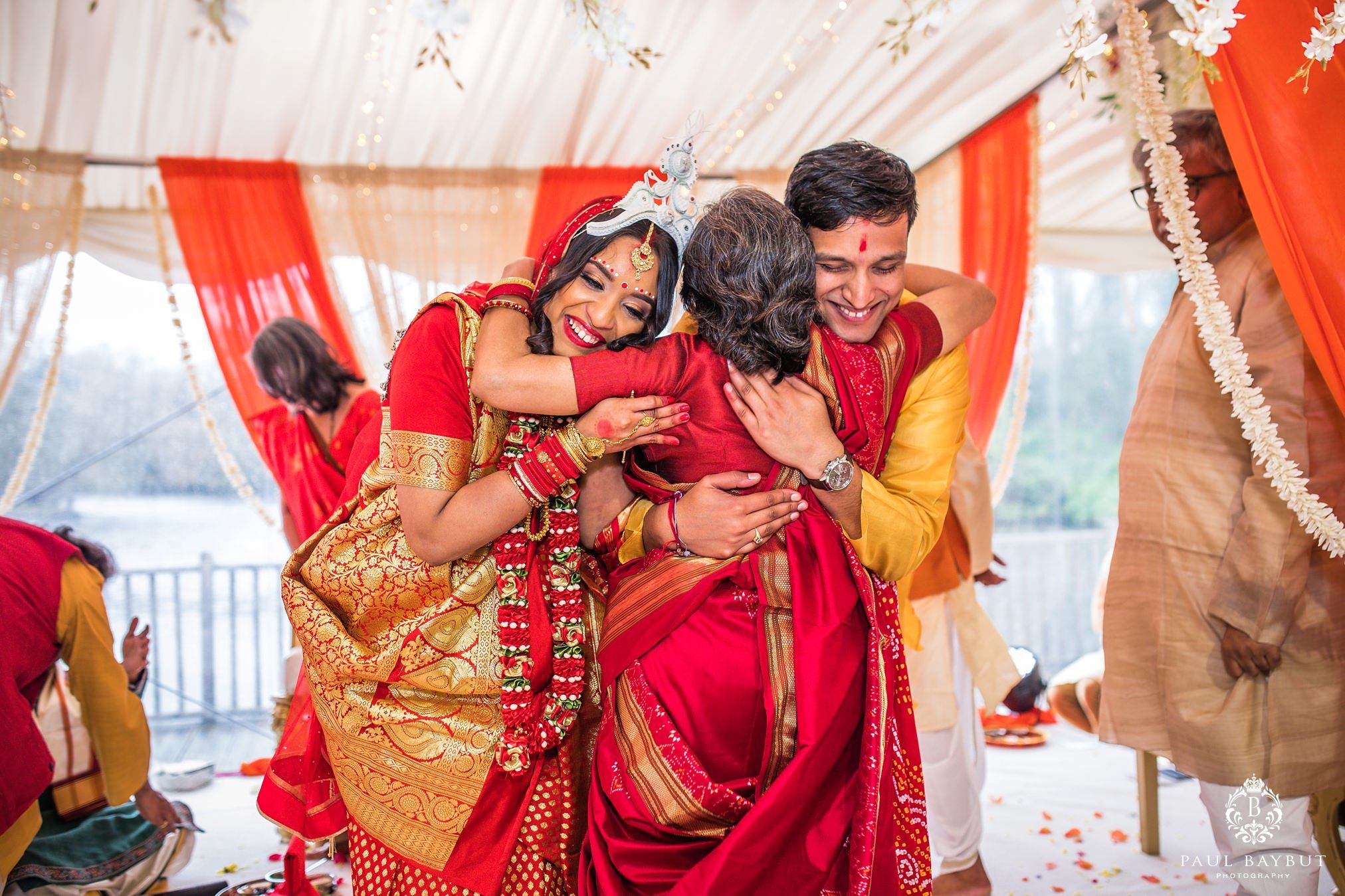 Newly weds both hug a female guest during their asian wedding ceremony at Thornton Manor Marquee