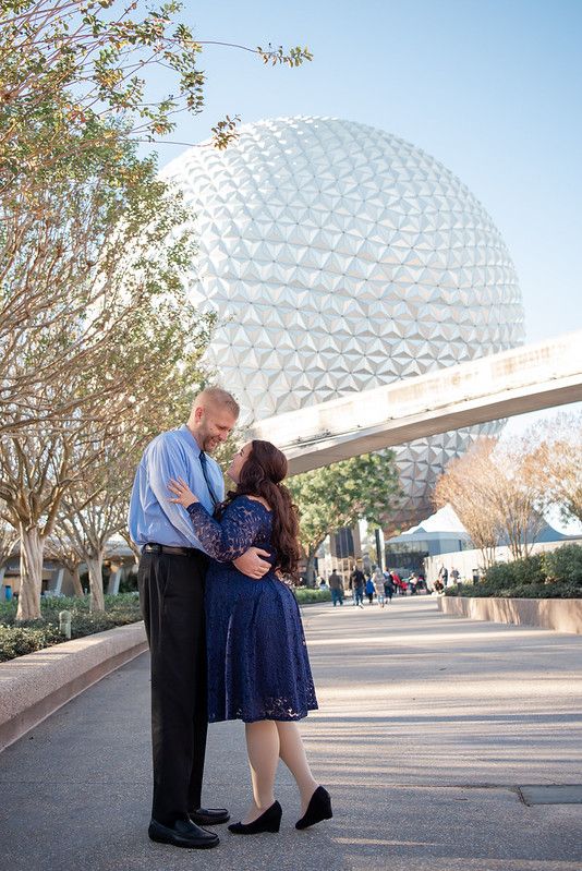 A couple standing in front of Spaceship Earth at Walt Disney World's Epcot in Orlando FL
