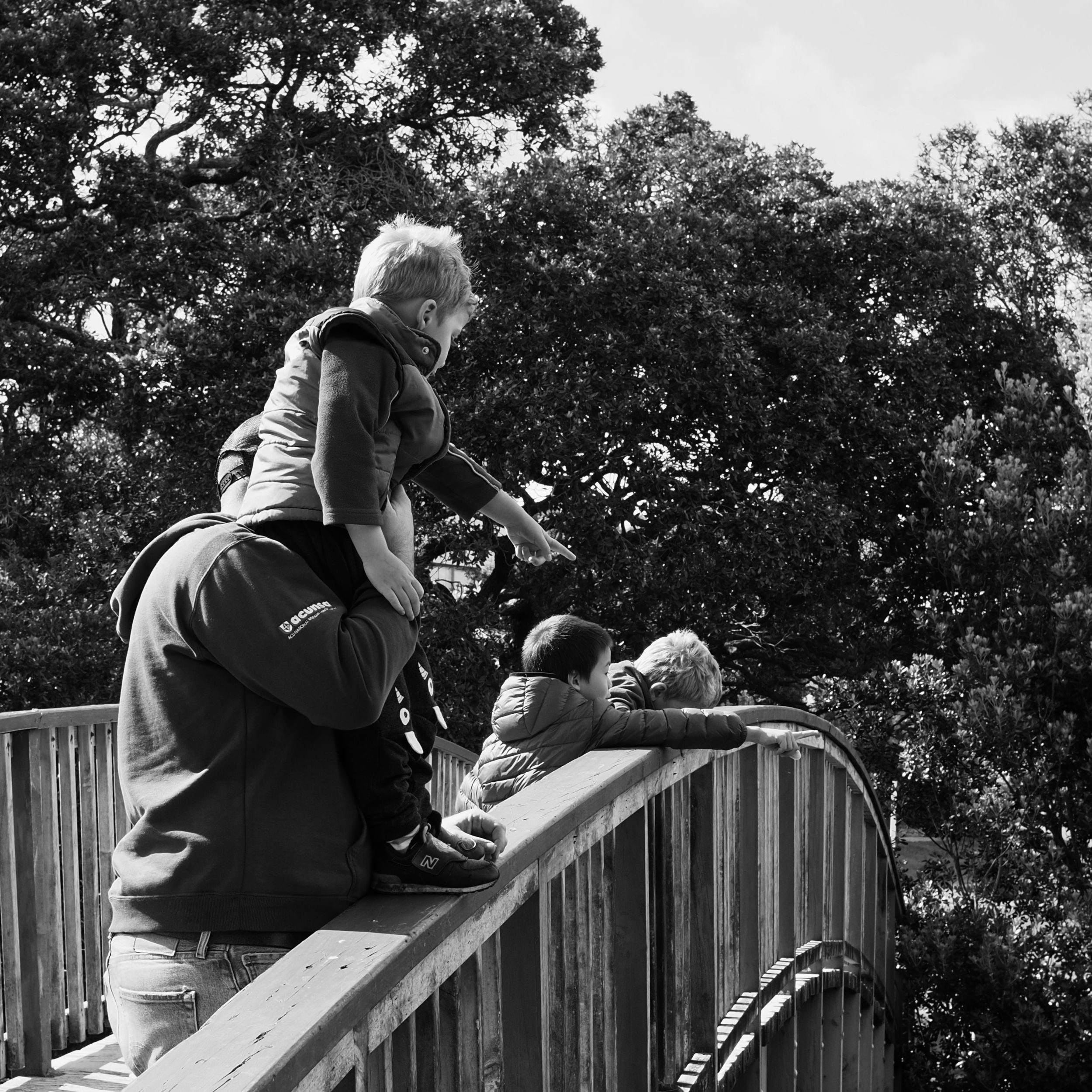 A black and white photo of the boys standing on a bridge pointing down at things floating in the estuary