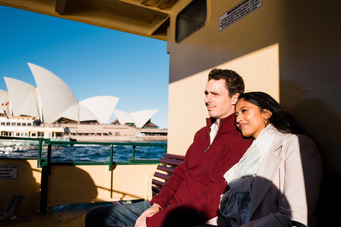 Woman resting her head on her partners shoulder on a ferry in Sydney with the Sydney Opera House in background