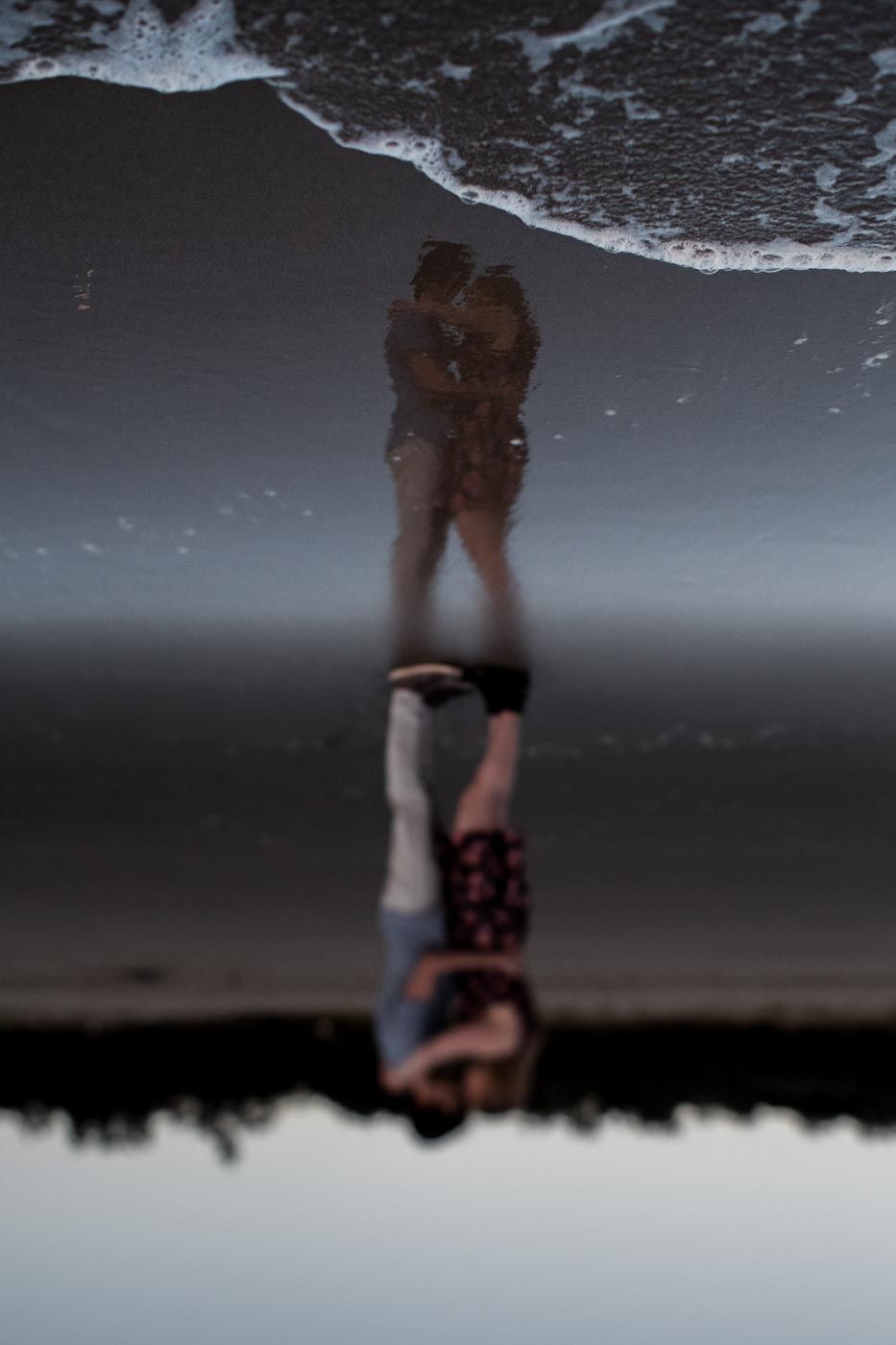 Reflection of a couple hugging at a beach in the early morning