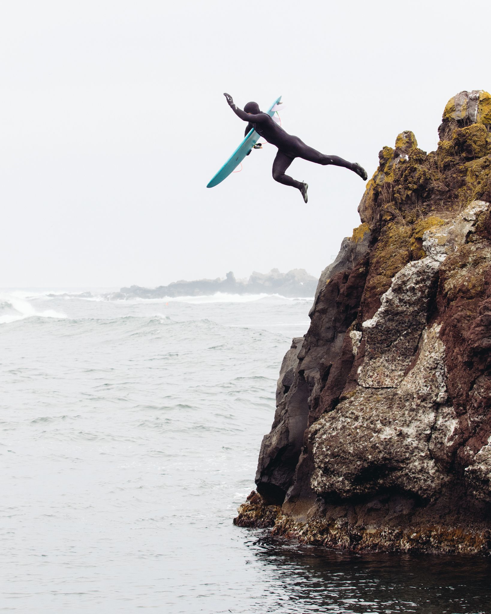 Surfer cliff jumping into the sea to cold water surf in Rishiri Japan