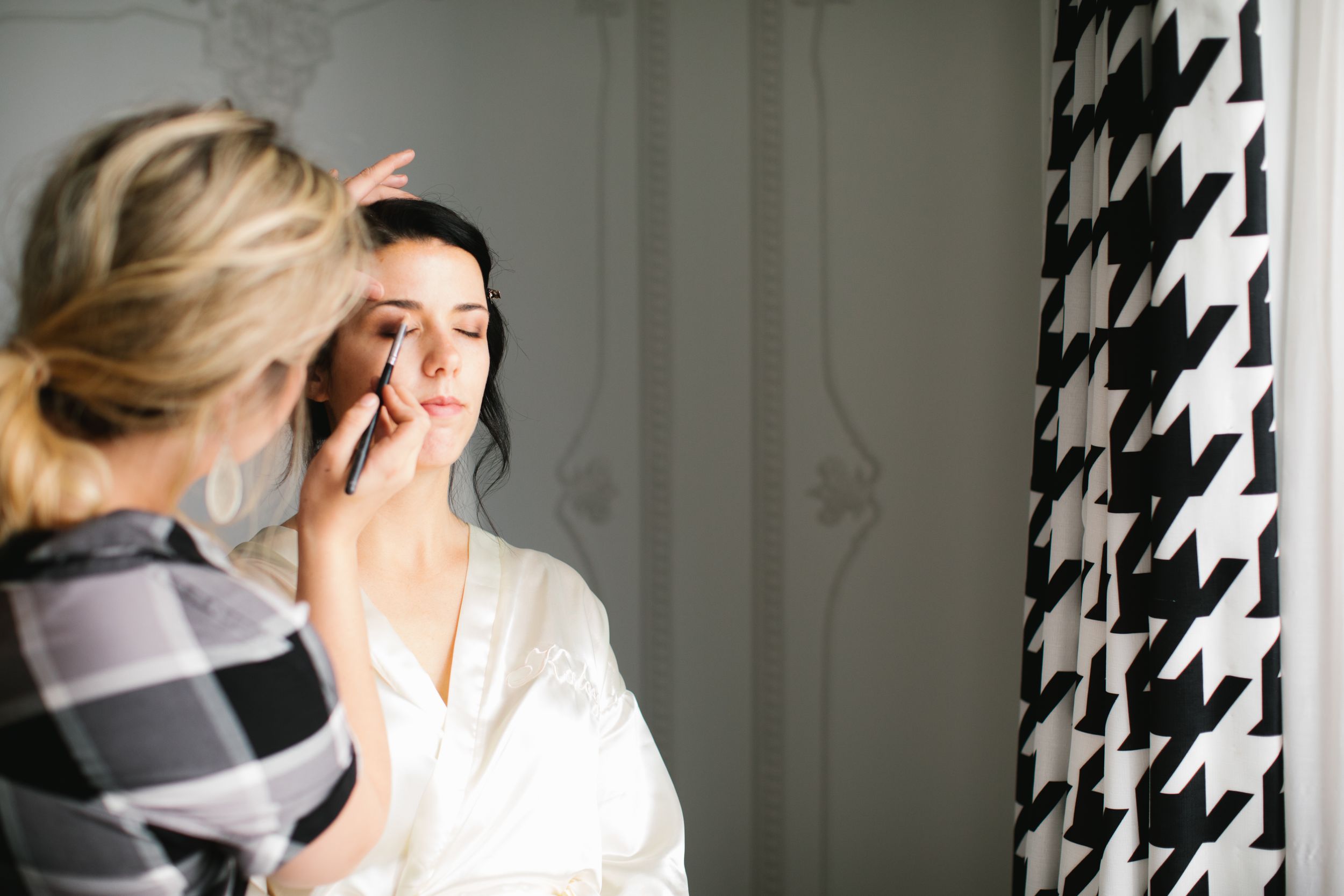 bride getting her makeup done in hotel room next to window