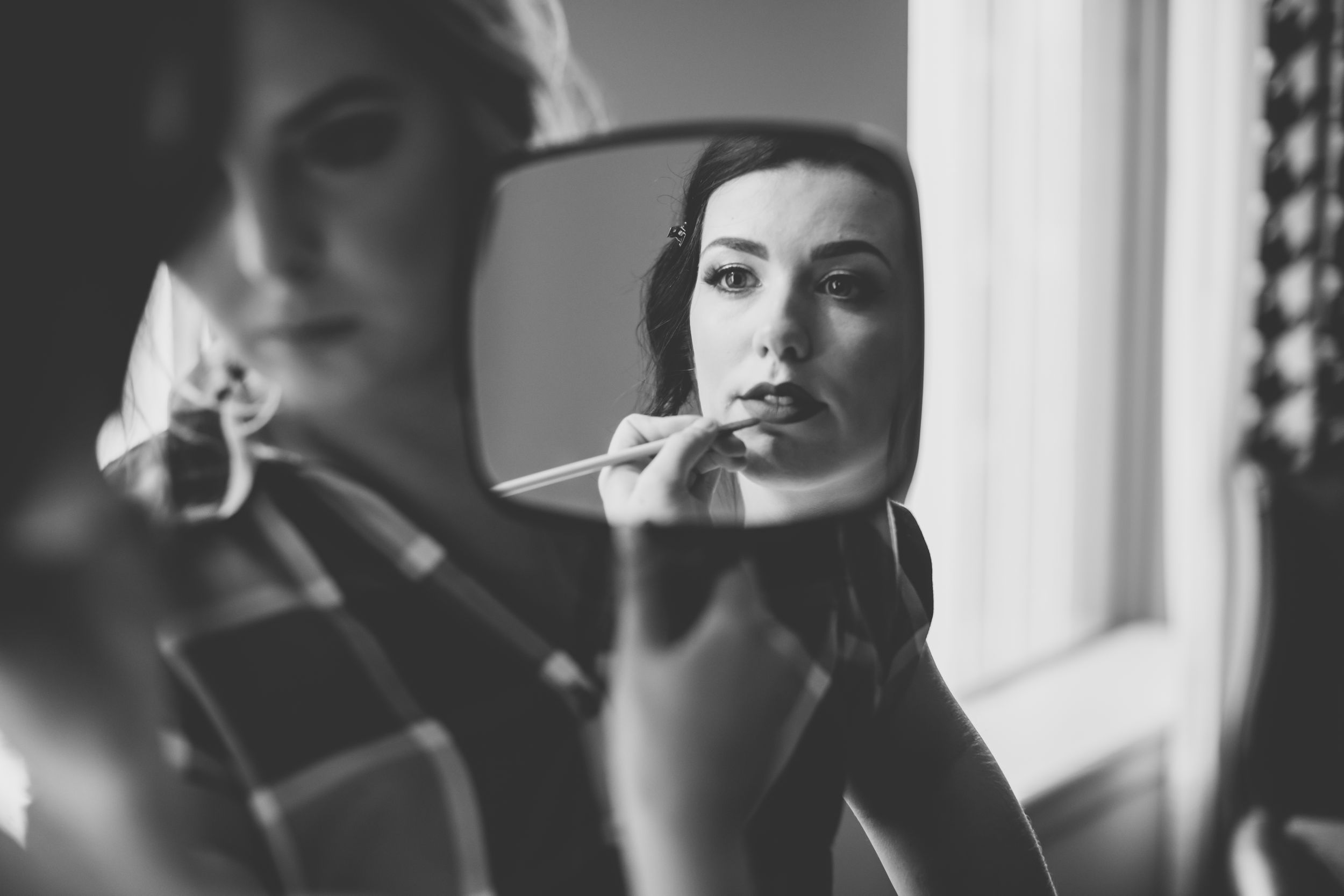 bride looking into hand mirror while makeup artist fixes her lipstick
