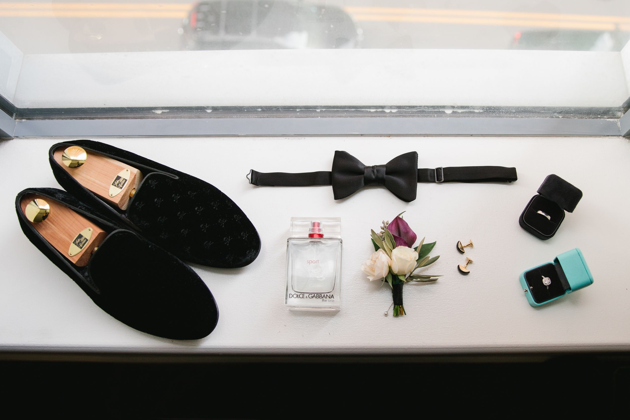 groomsman details flatlay - shoes, boutonniere, cologne, cufflinks, rings.