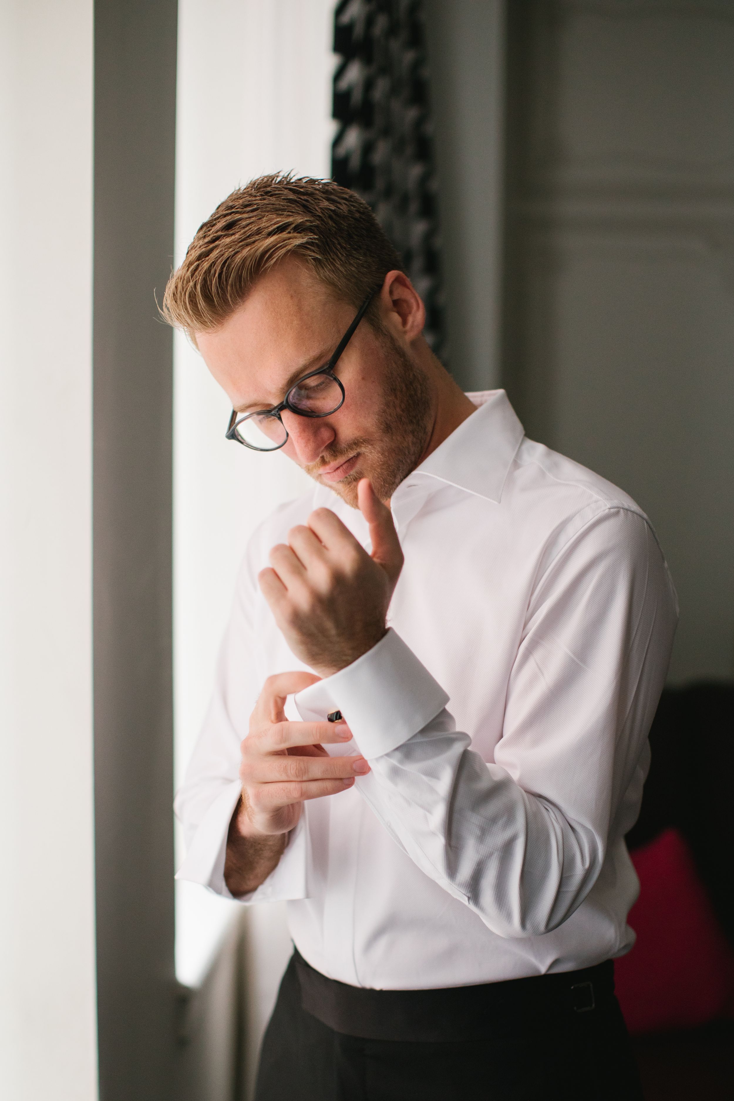 groom putting on cuff links next to window