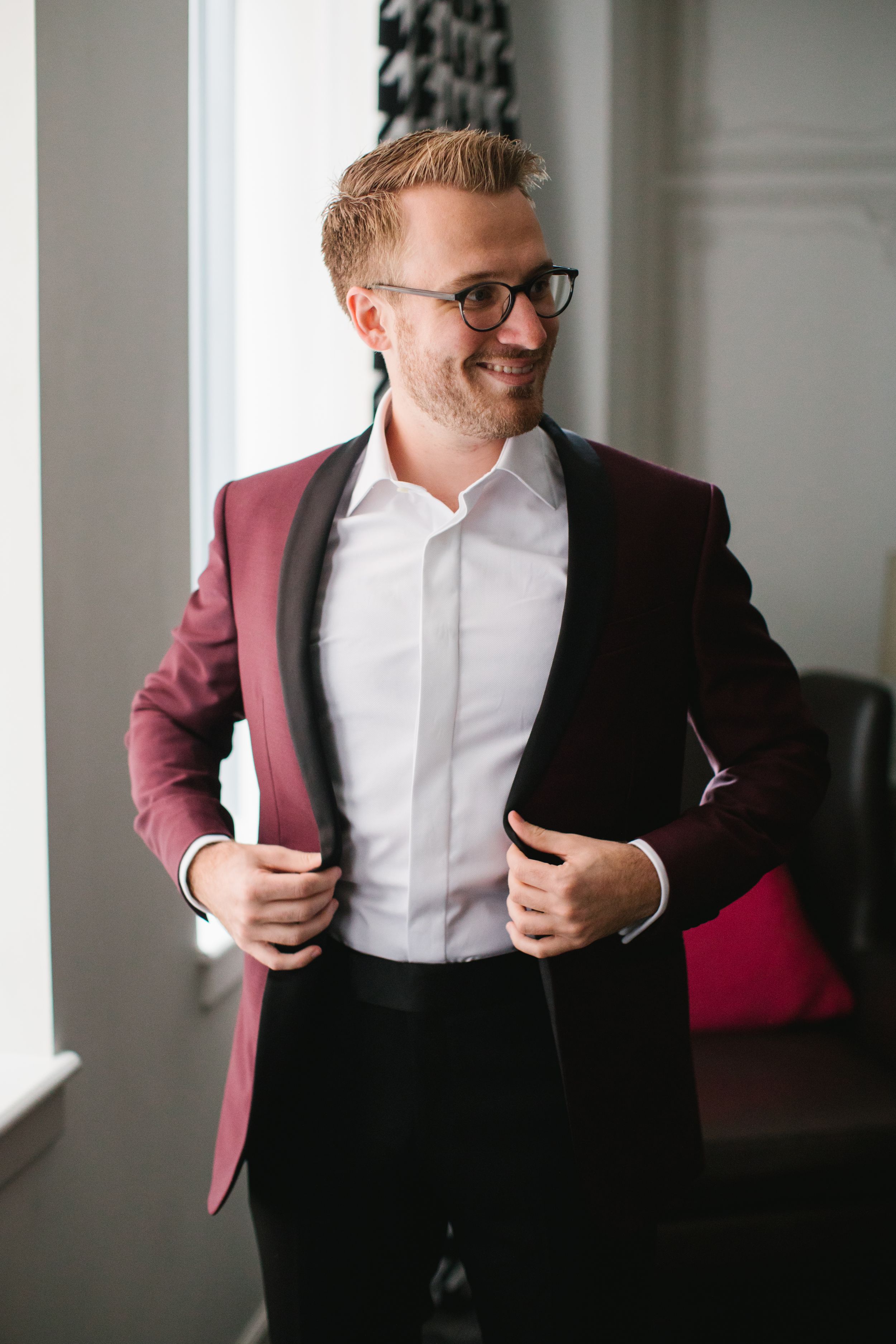 groom putting on suit jacket and laughing by window