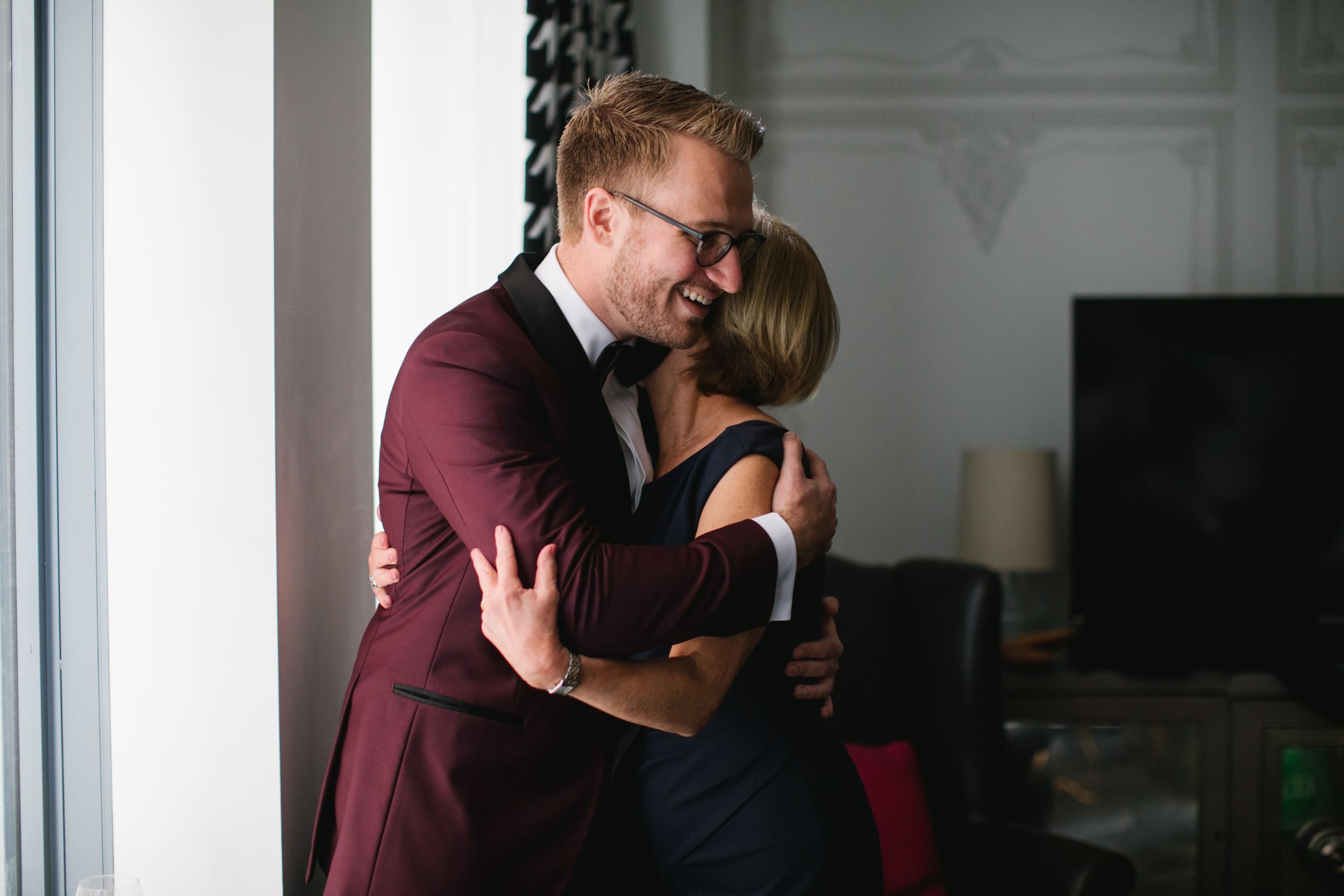 mother of groom hugging him and laughing by window