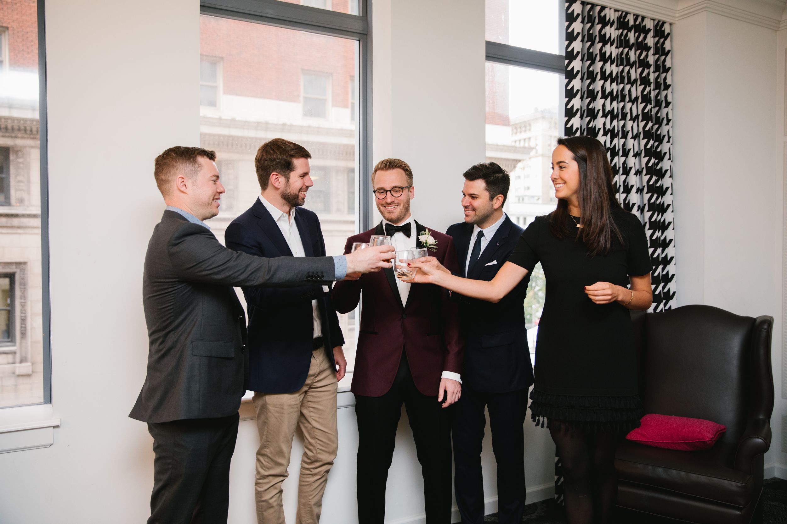 groom and friends do a cheers with whiskey glasses in hotel room