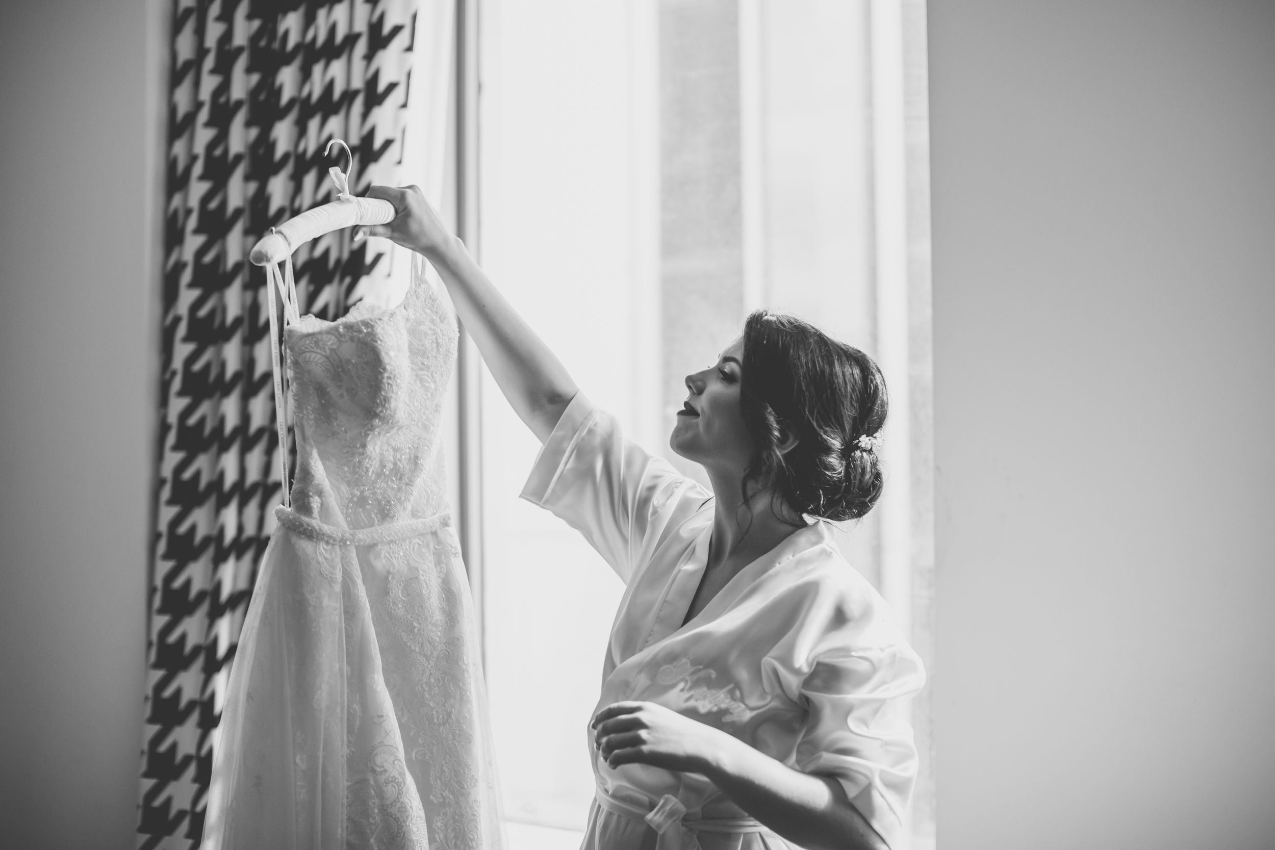 bride holding up wedding dress in front of window black and white