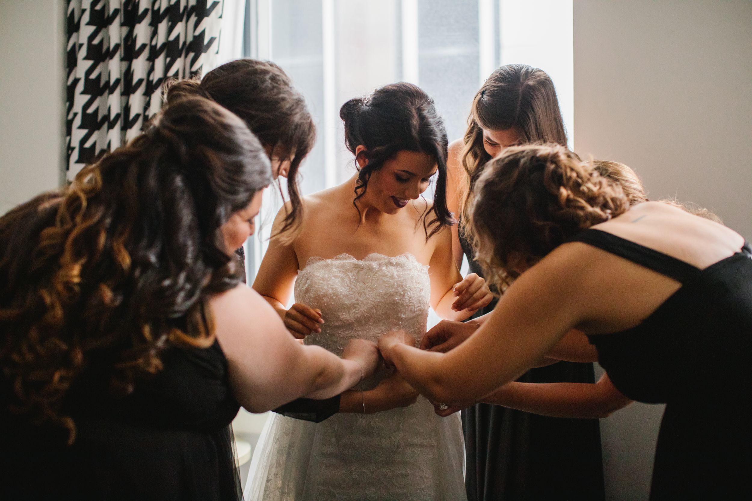 bridesmaids helping put on wedding skirt in front of window