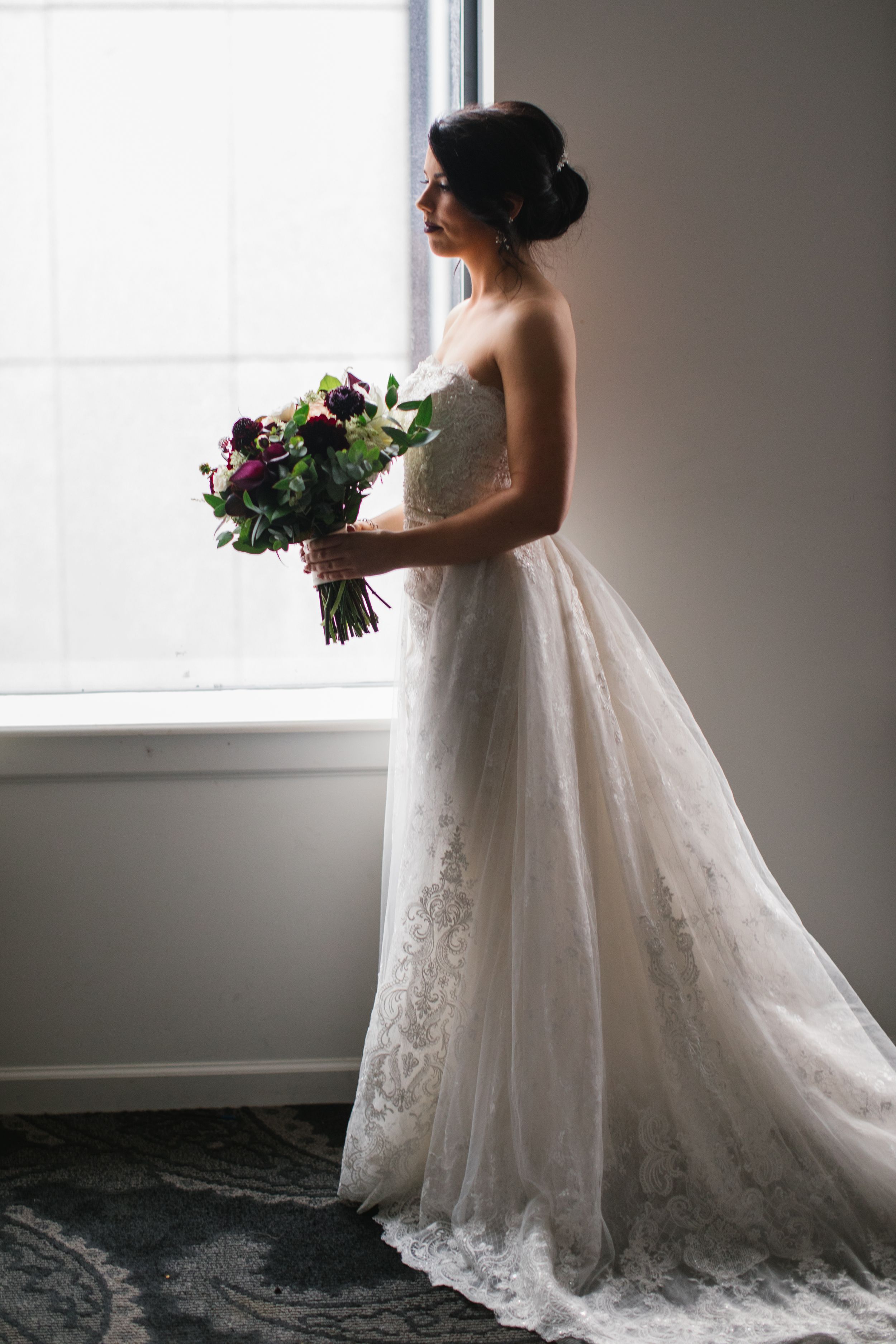 side profile of bride in her wedding dress by window with bouquet