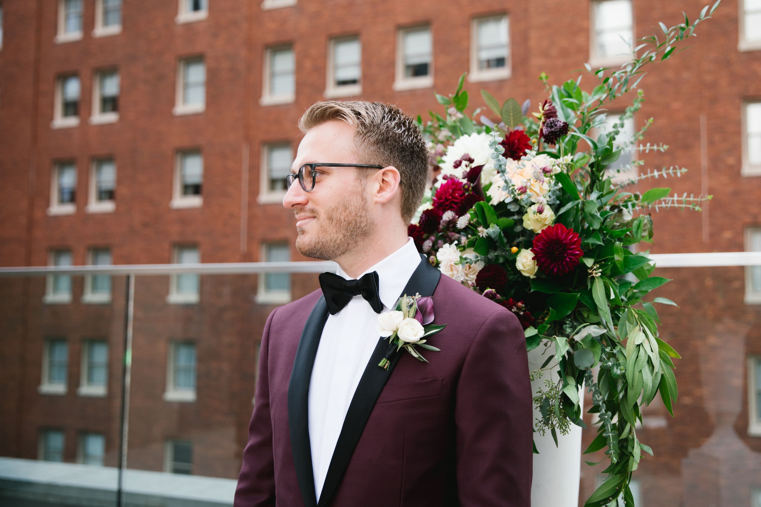 groom looking at bride walking down the aisle with building behind him