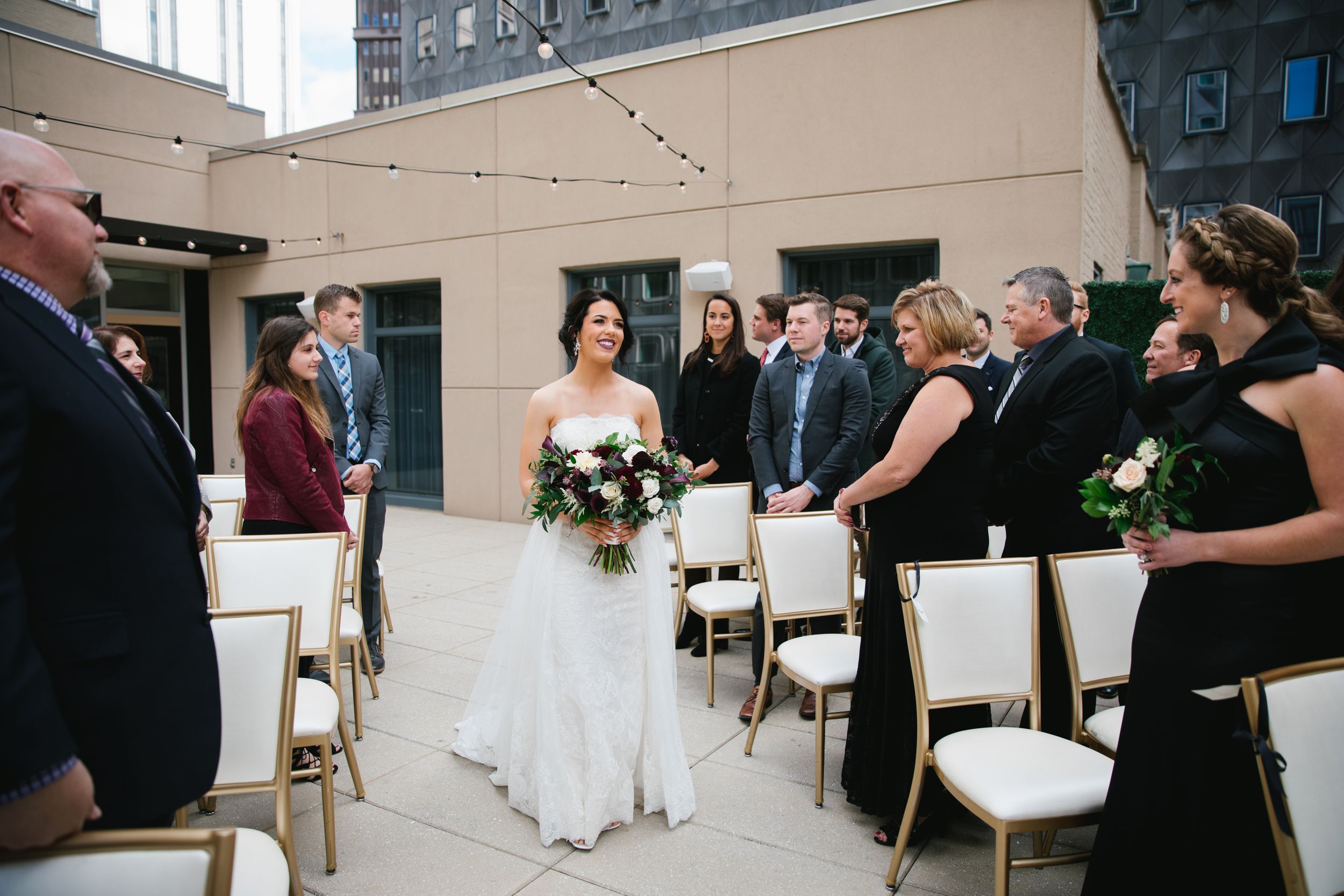 bride walking down aisle smiling with friends and family looking on