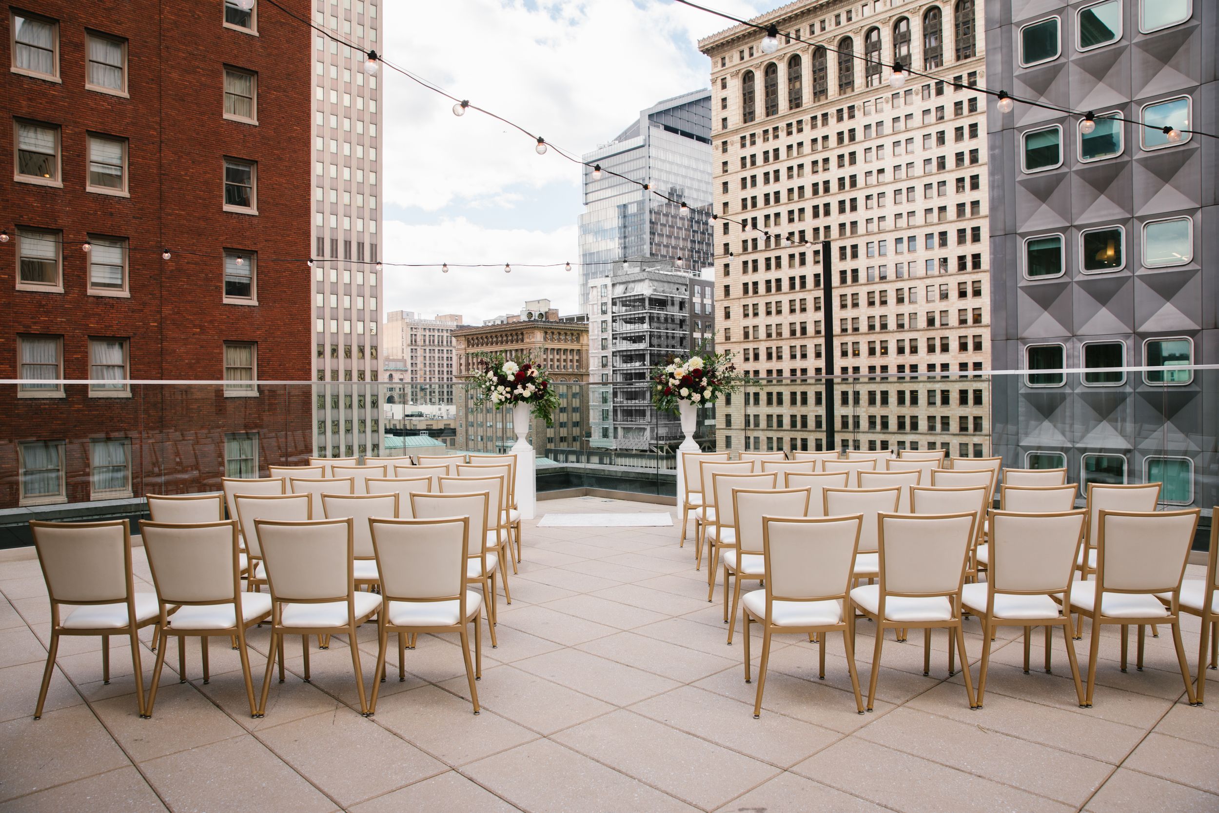 rooftop ceremony space overlooking the city with high rise buildings with string lights, column planters and gold chairs