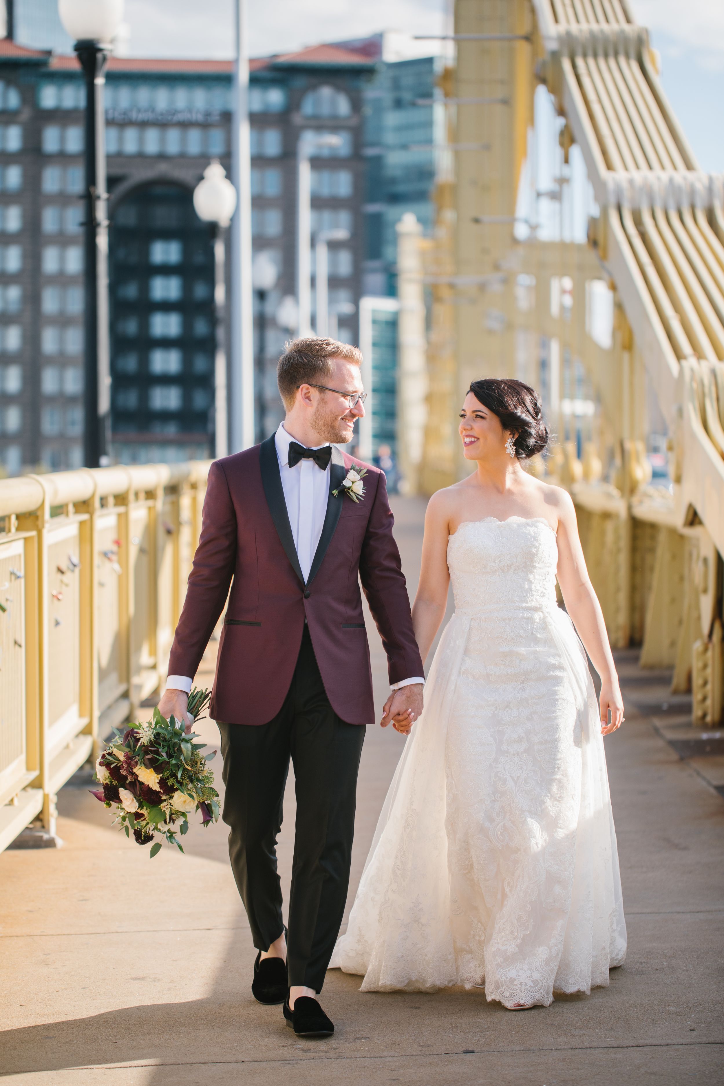 bride and groom walk on yellow bridge in pittsburgh city