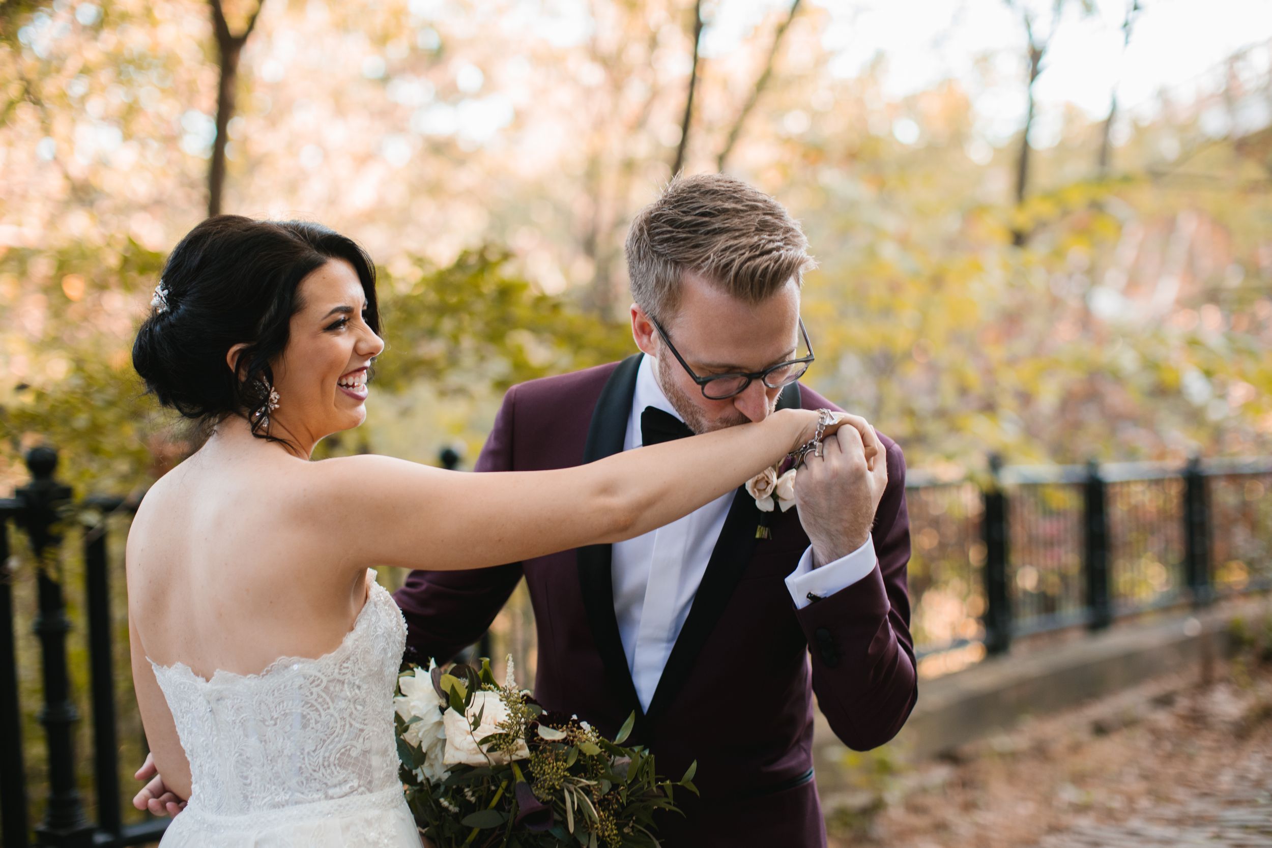 groom kissing brides hand while she laughs in park during fall