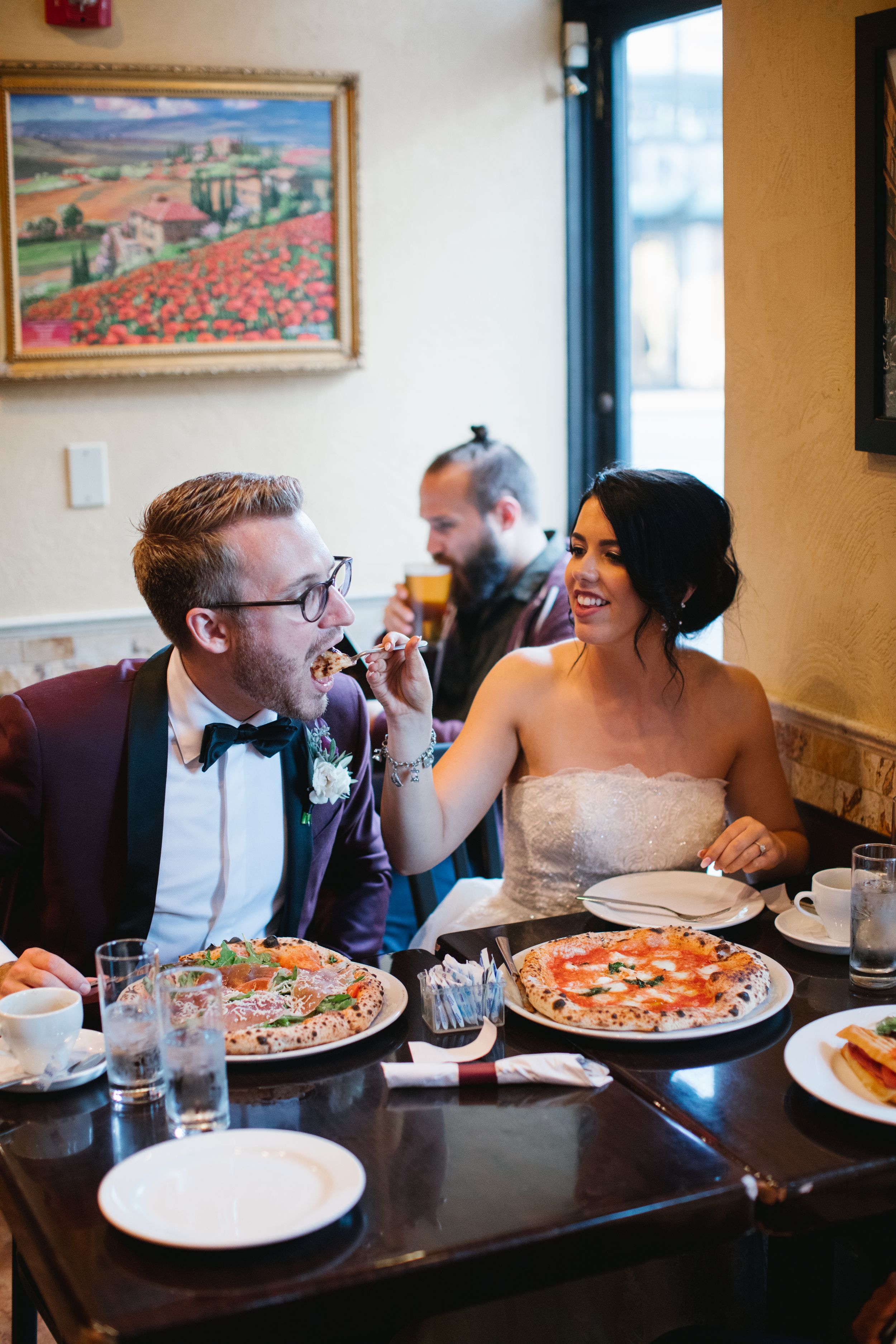 bride and groom feeding each other pizza and laughing