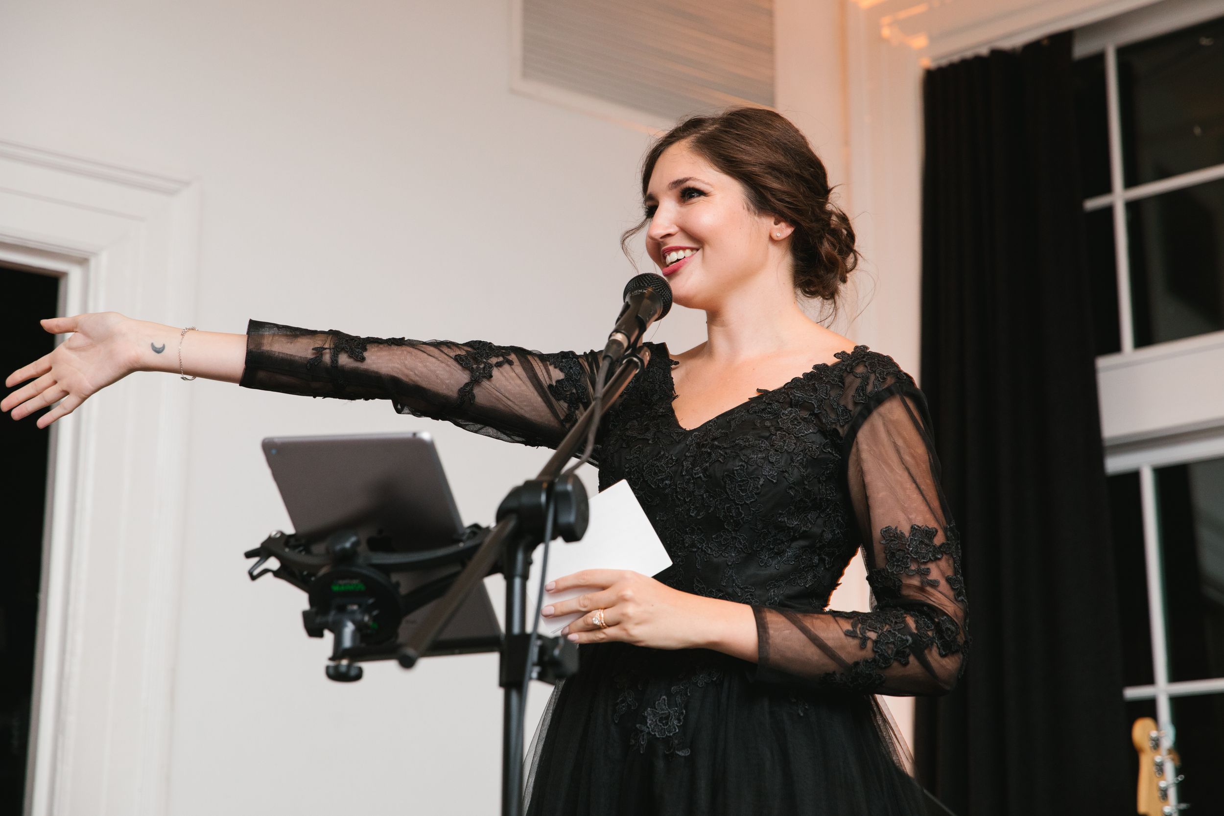 maid of honour in black dress making speech and pointing at bride and groom