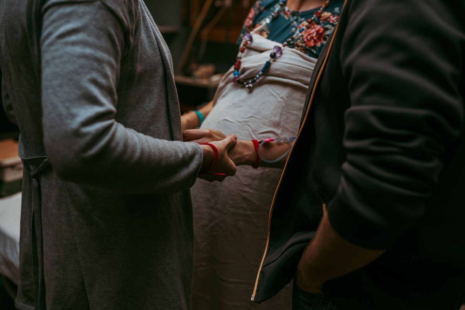 A pregnant woman holding hands with her doula showing both of their prayer bracelets.