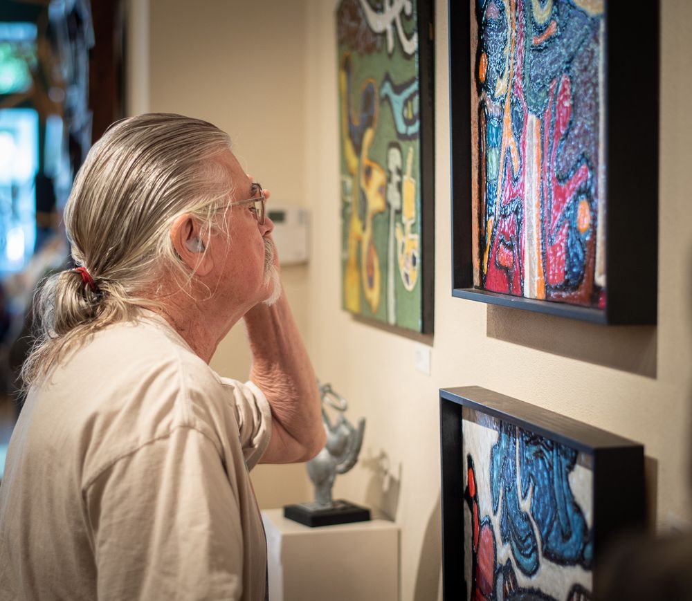 Older man with ponytail peering at a painting on a wall.
