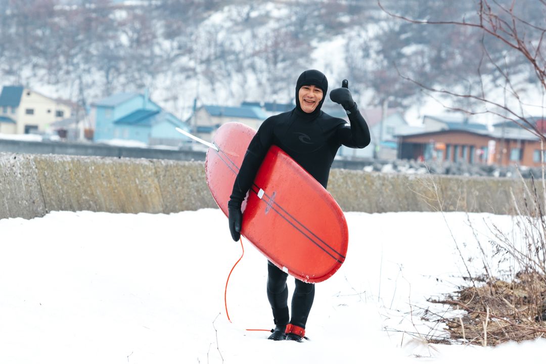 Hideki Yamanaka smiling face thumbs up with a longboard surfboard in winter Japan