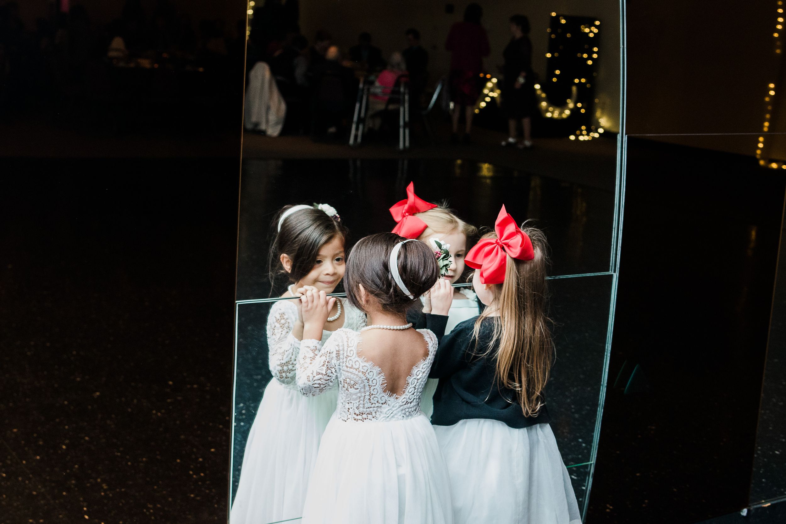 Young girls stare into mirrored wall at wedding reception by Hudson Valley photographer