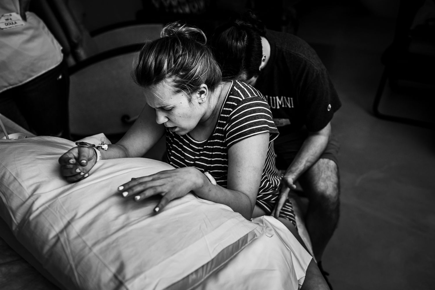 A black and white image of a woman sitting on a birth ball as her husband sits behind her applying pressure to her hips.