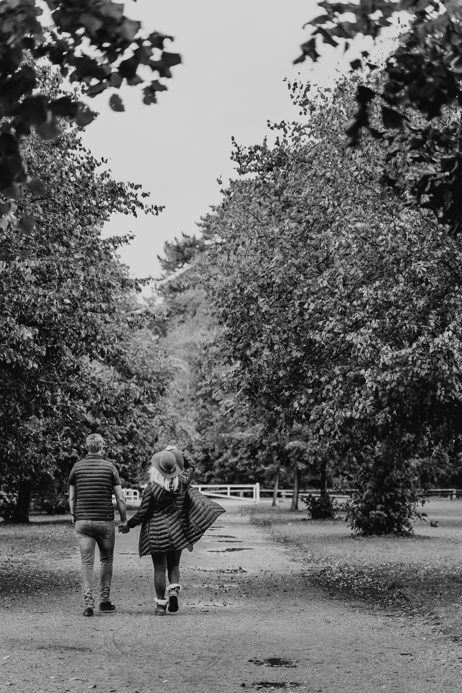 Black and white image of a couple walking away down a park path. Katherine and her Camera engagement photoshoot.