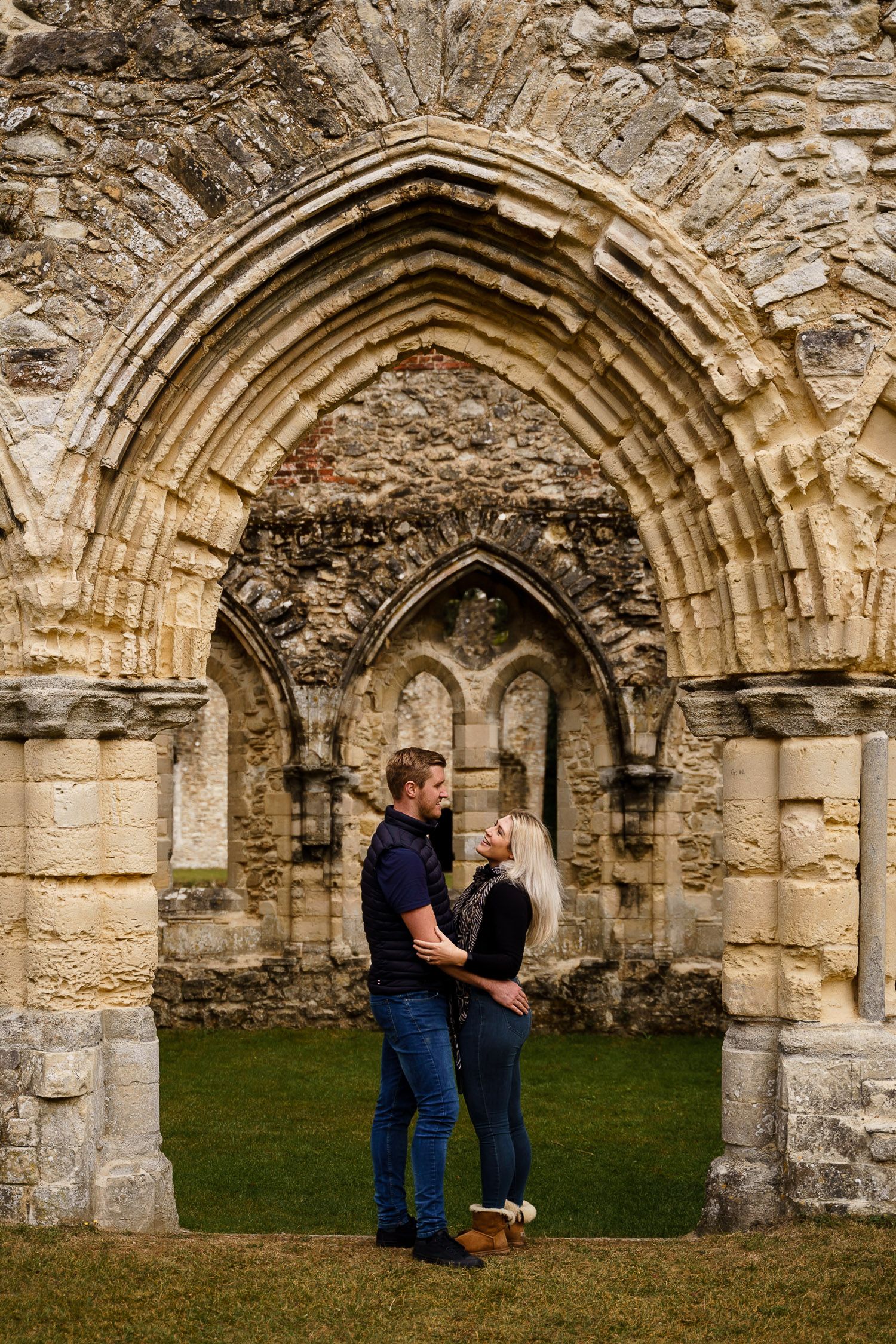 Portrait of couple laughing together framed by an arch in Netley Abbey. Katherine and her Camera engagement photoshoot.