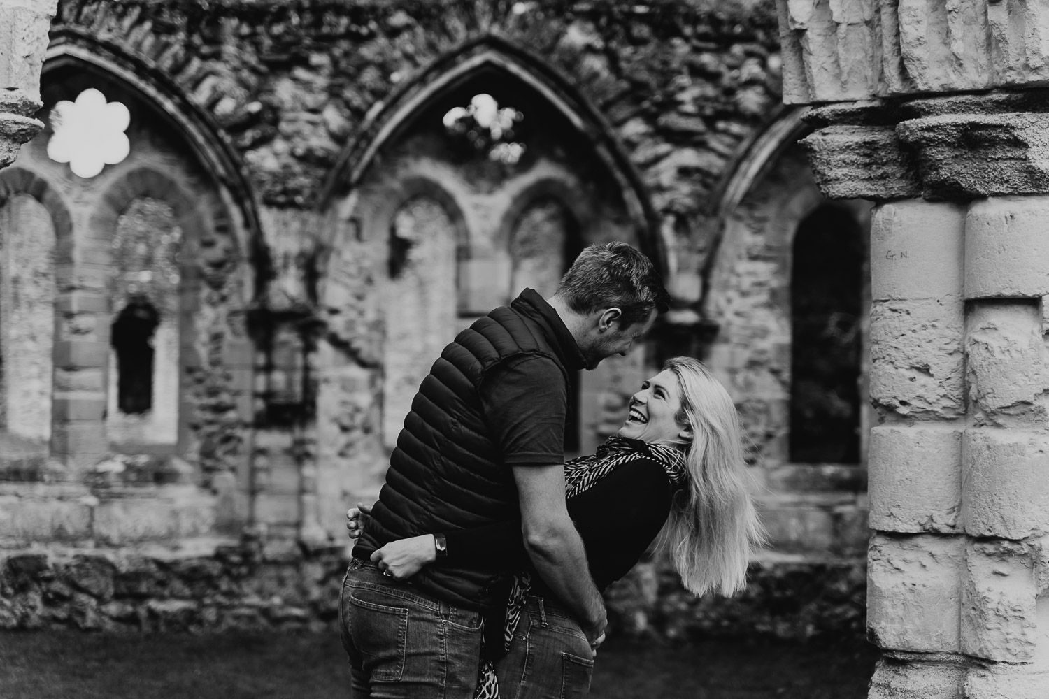 Black and white image of a couple laughing and playing in Netley Abbey. Katherine and her Camera engagement photoshoot.