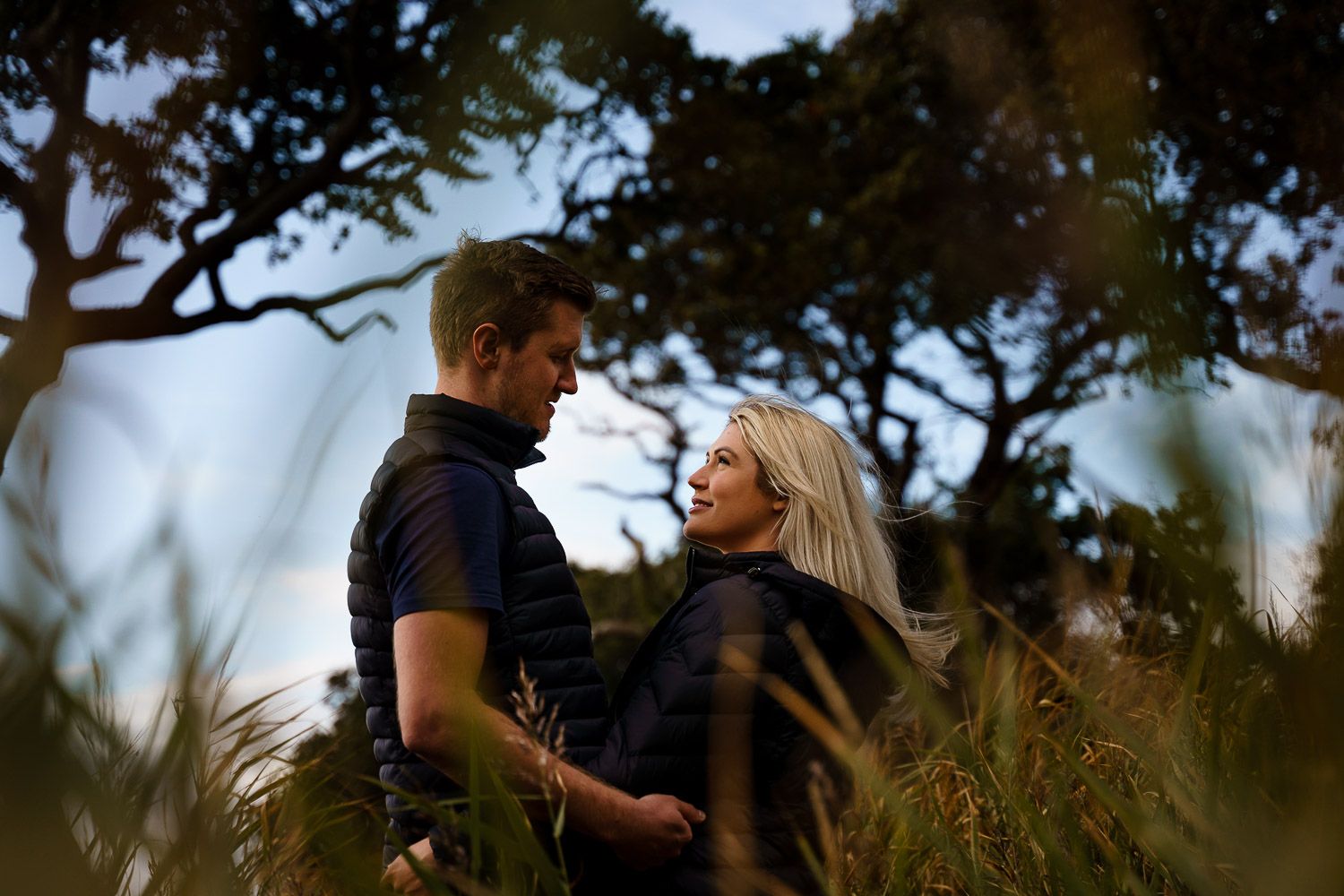 Engaged couple look into each other's eyes, framed by long grass. Katherine and her Camera engagement photoshoot.