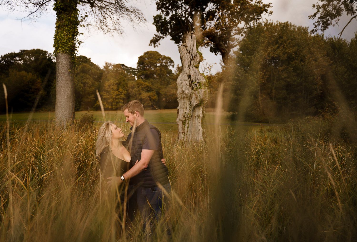 Couple gaze into each other's eyes framed by long grass. Katherine and her Camera engagement photoshoot.