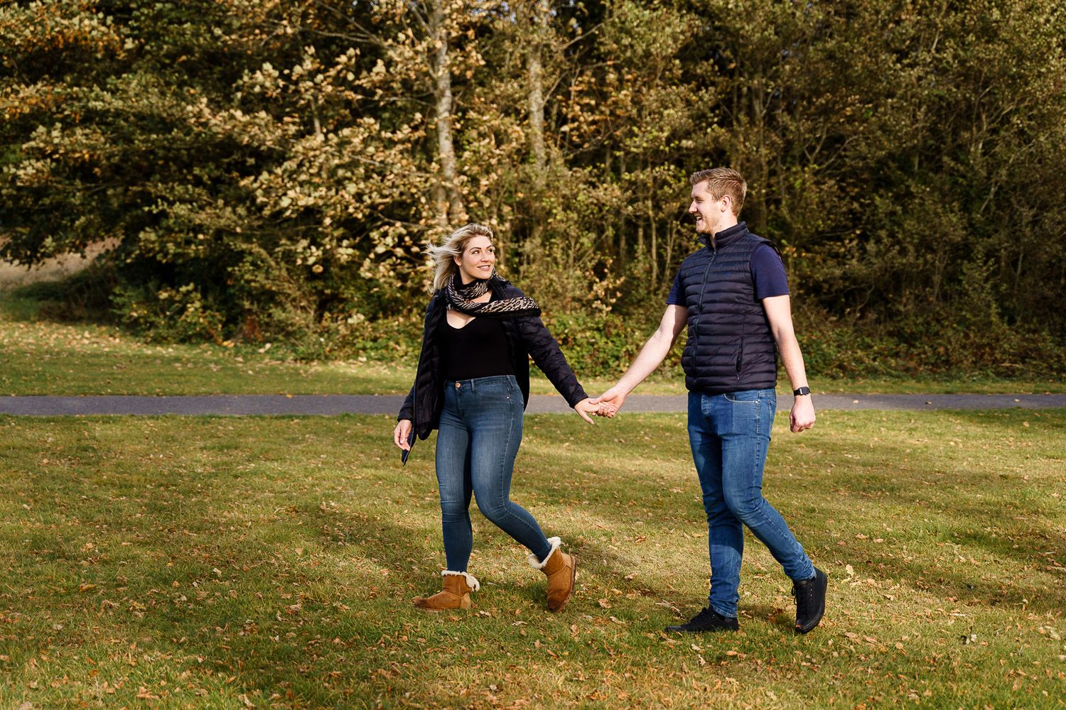Bride to be walks across a park leading her fiance by the hand. Katherine and her Camera engagement photoshoot.