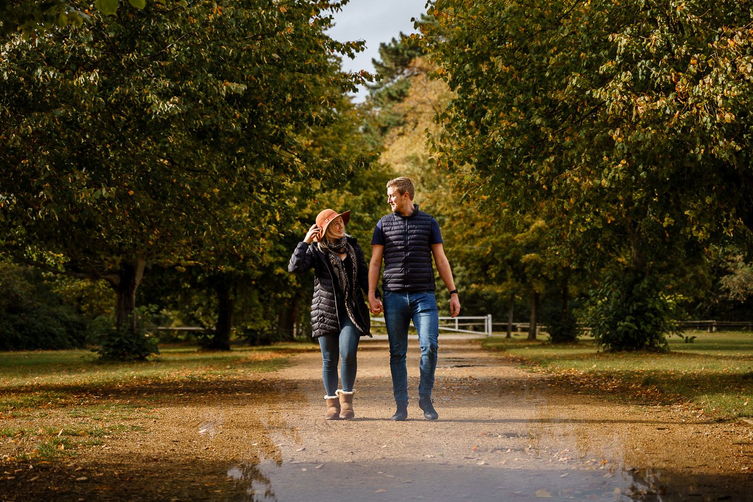 Couple walk towards the camera holding hands in an autumnal park. Katherine and her Camera engagement photoshoot.